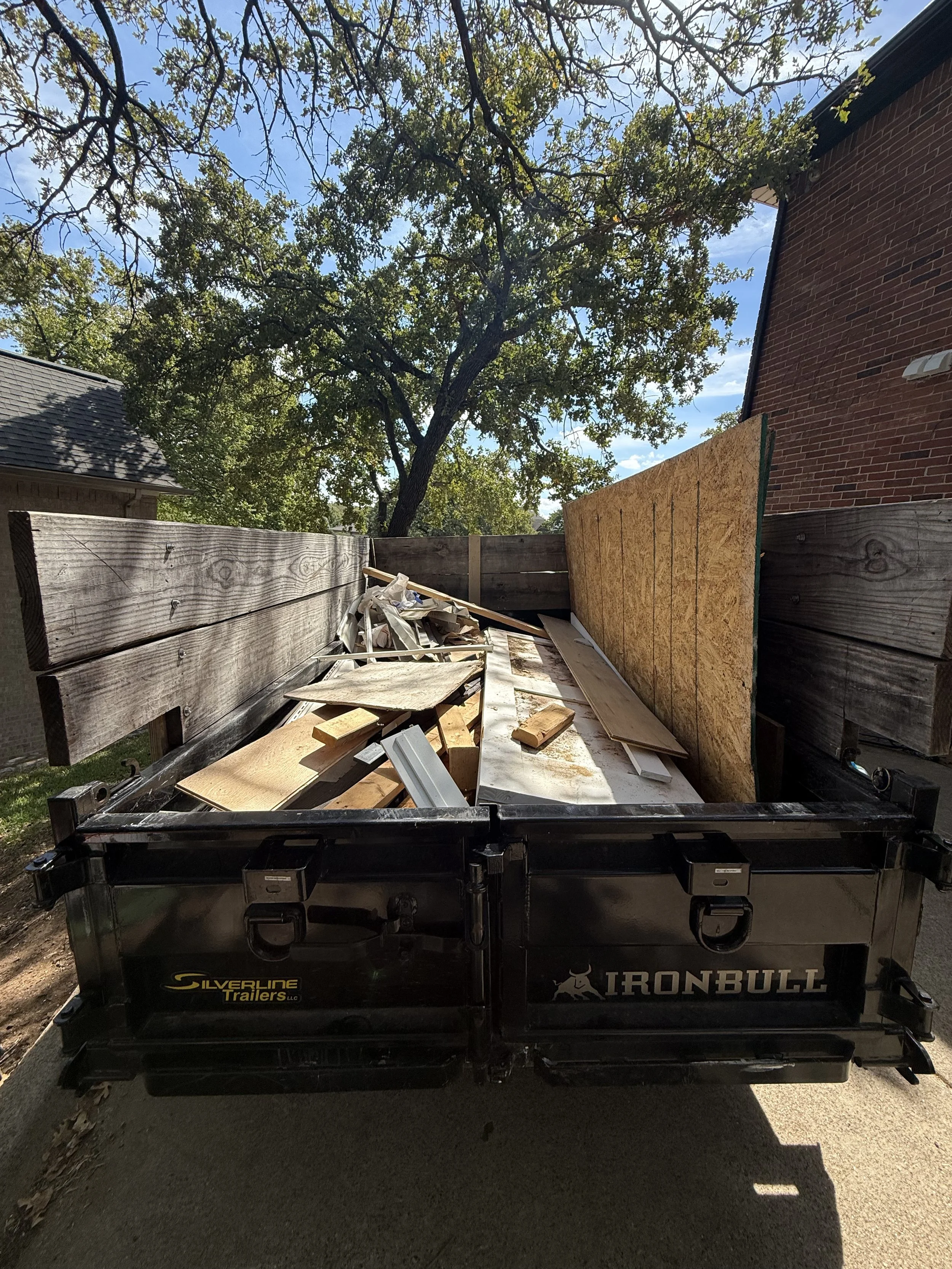 A trailer on a road carrying a large load of white tarps, wooden planks, and construction materials.