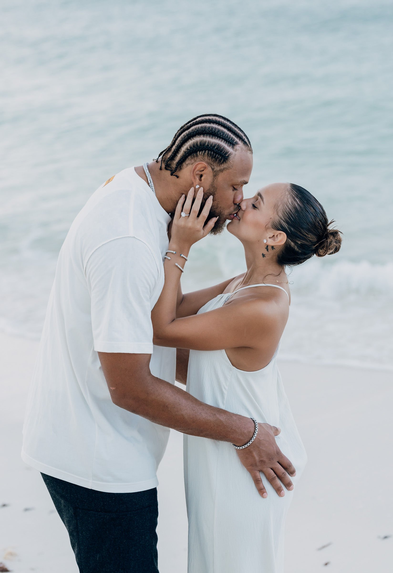 A couple sharing a kiss on the beach with the ocean in the background.