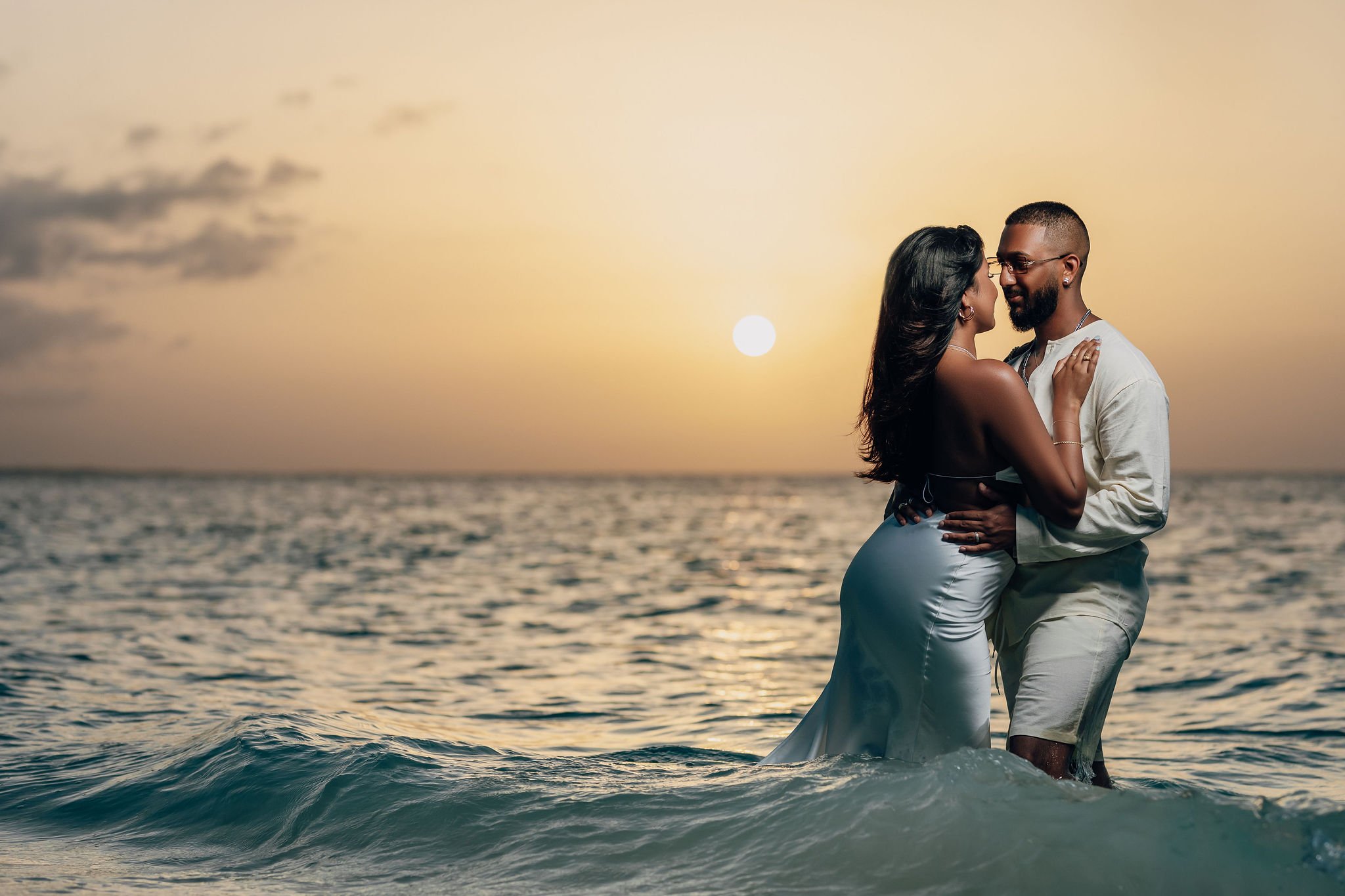 A couple standing in the ocean during sunset, embracing each other affectionately.