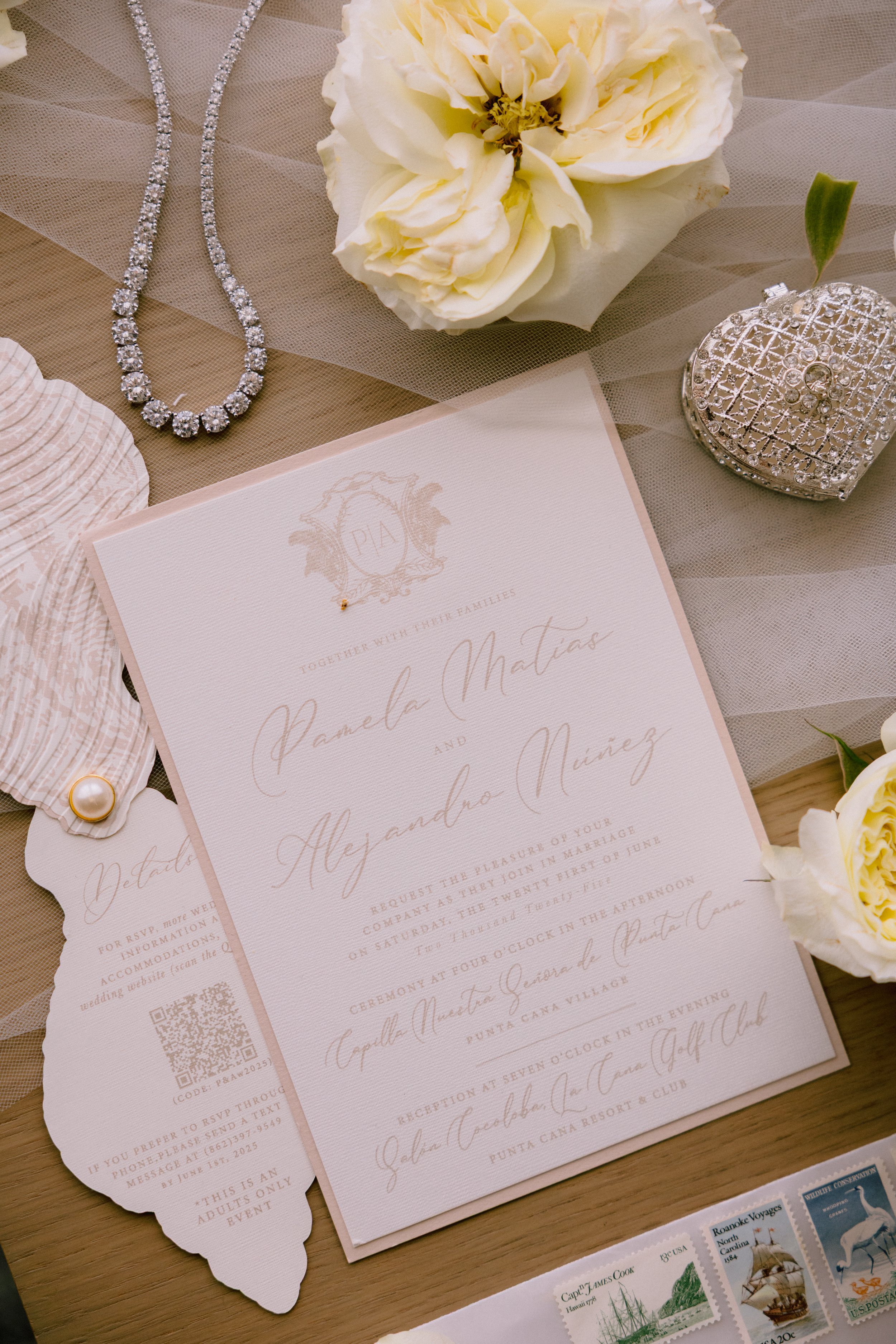 Wedding invitation with white roses, jewelry, and decorative items on a table.