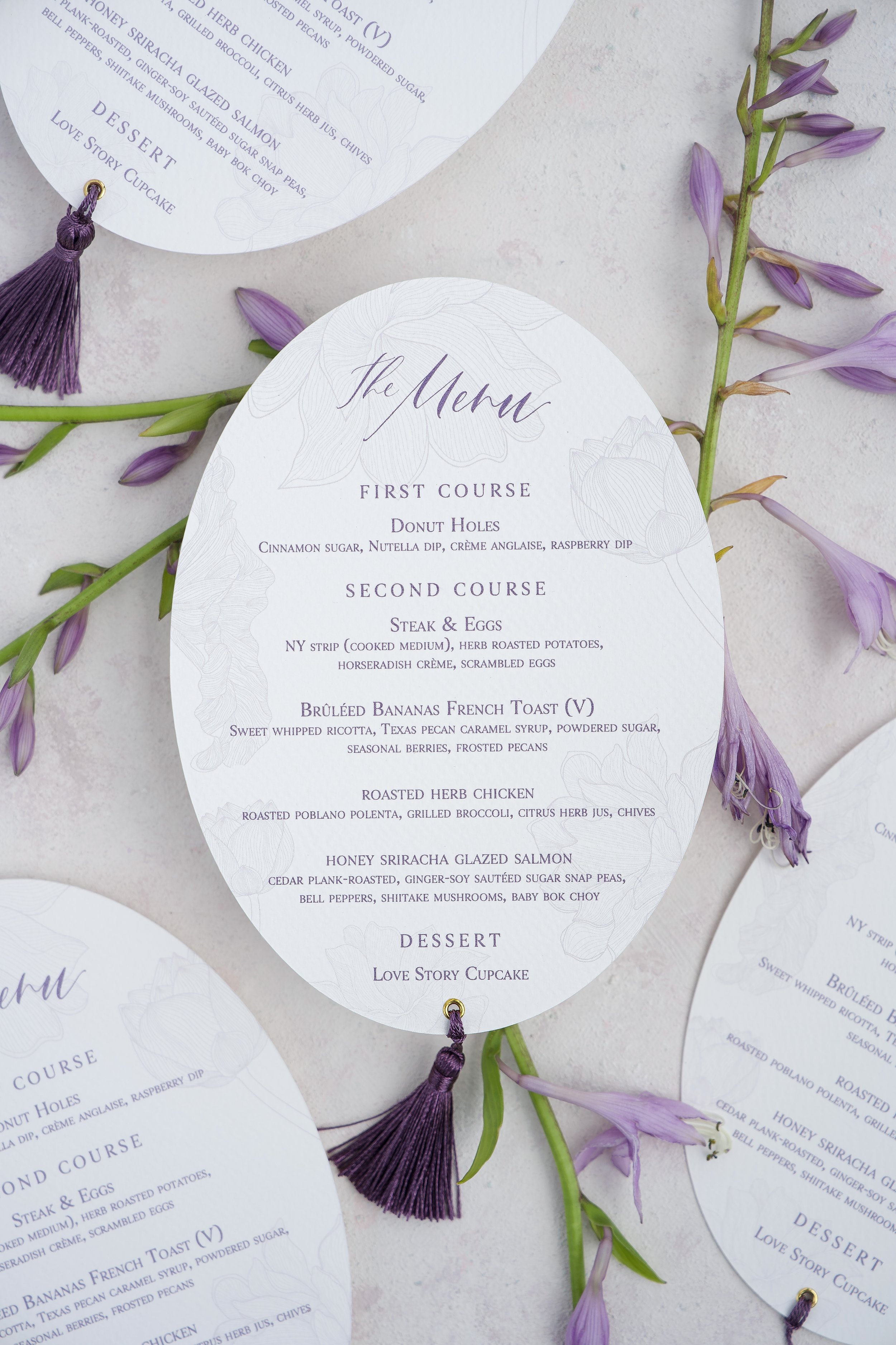 Elegant wedding menu card with floral design, listing first course of donut holes, second course of steak and eggs, roasted herb chicken, and honey sriracha glazed salmon, followed by dessert 'Love Story Cupcake', decorated with purple flowers and pu