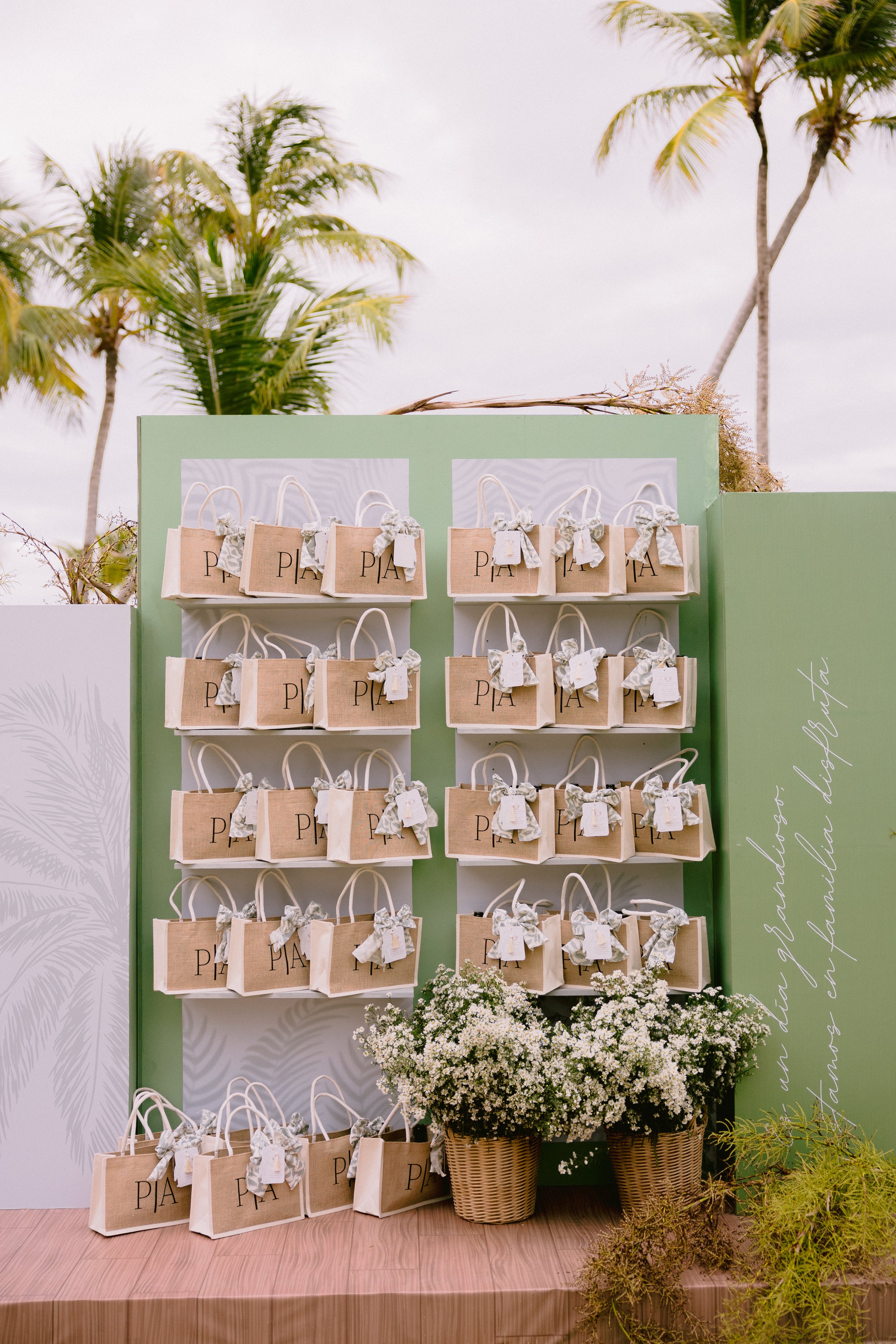 Display of small gift bags labeled 'PIA' arranged on a board with white flowers and palm trees in the background.