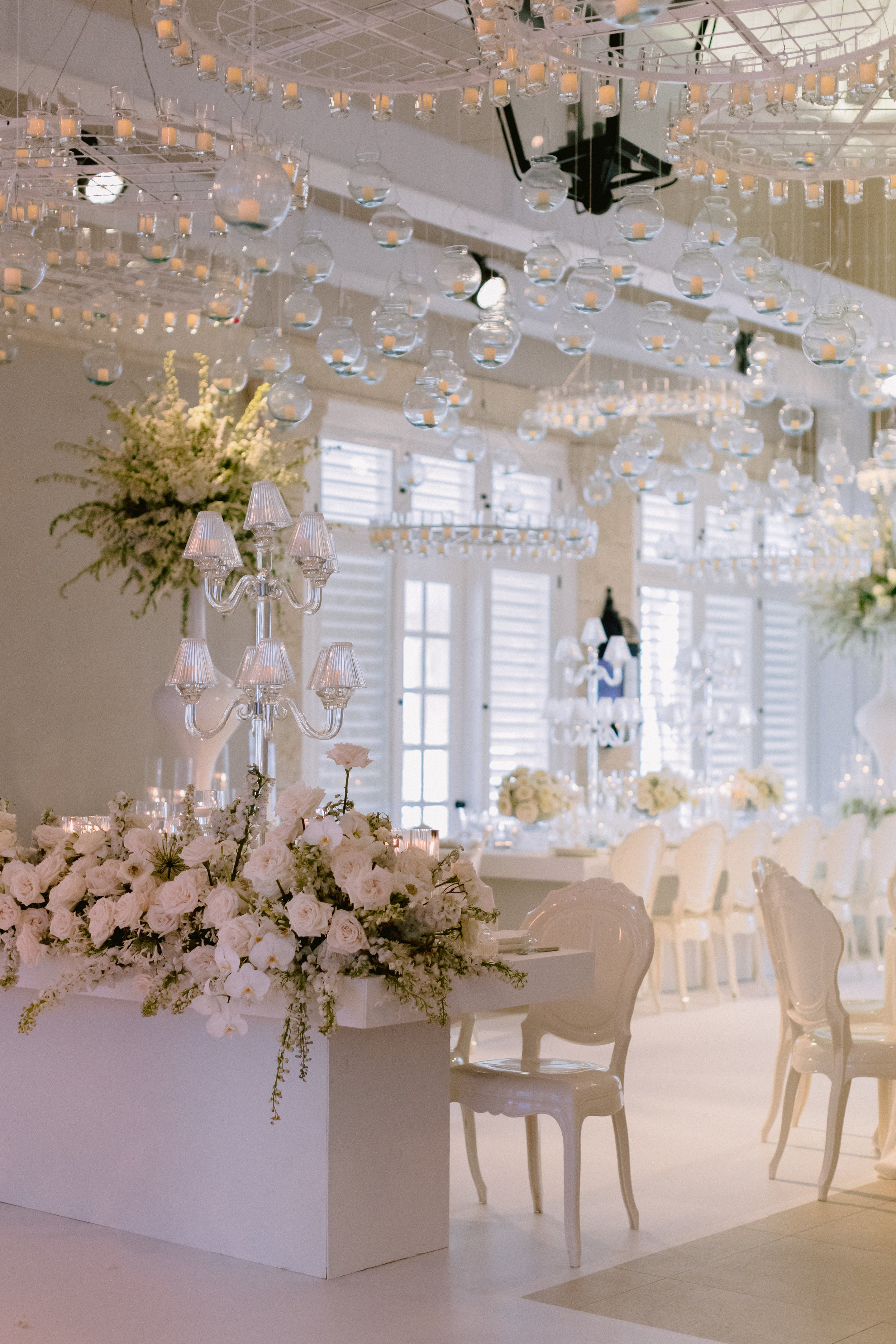 Elegant wedding reception hall decorated with white flowers, chandeliers, and candles.