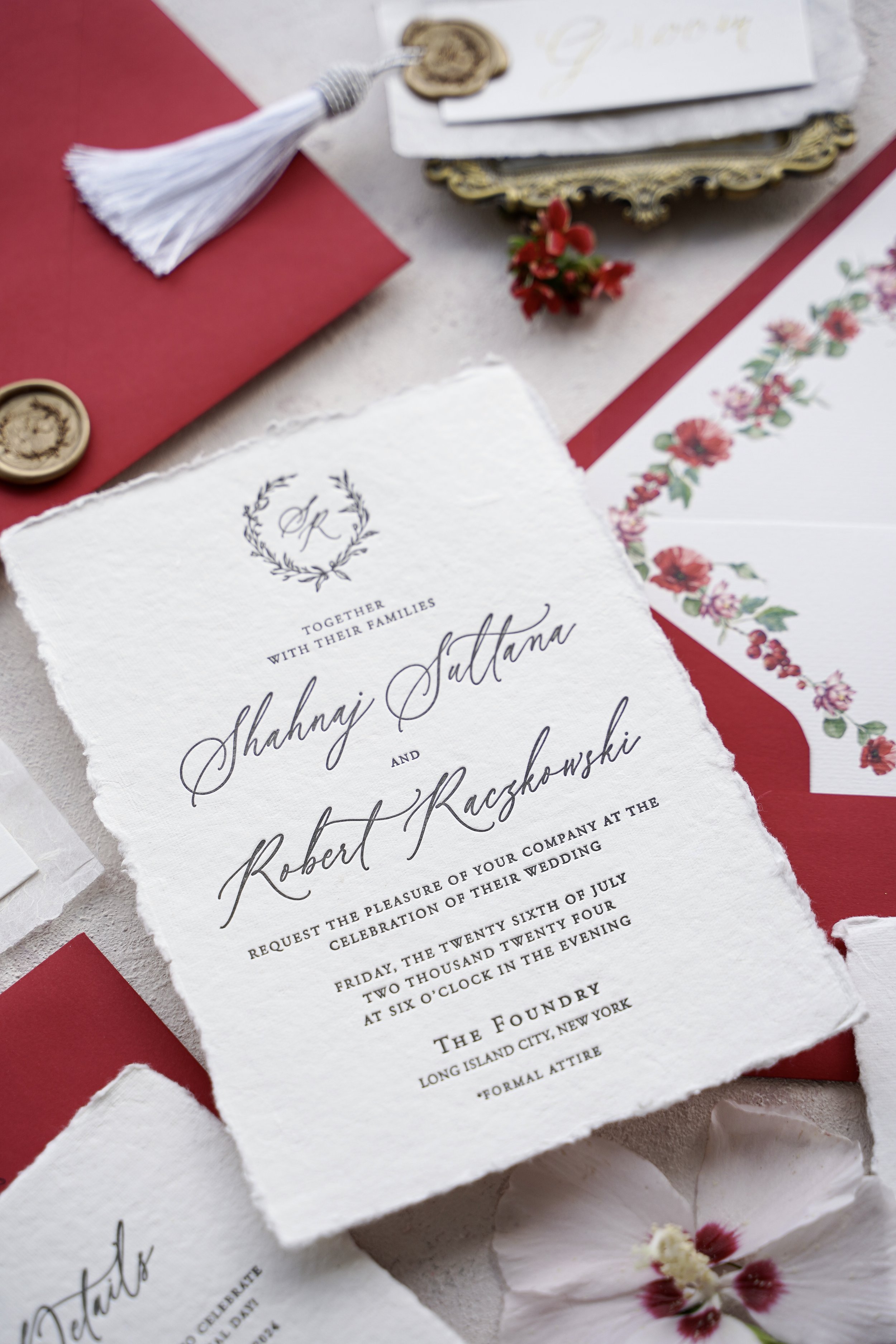 Elegant wedding invitation with handmade paper, calligraphy, and floral details, surrounded by red and white envelopes, wax seals, and decorative flowers.