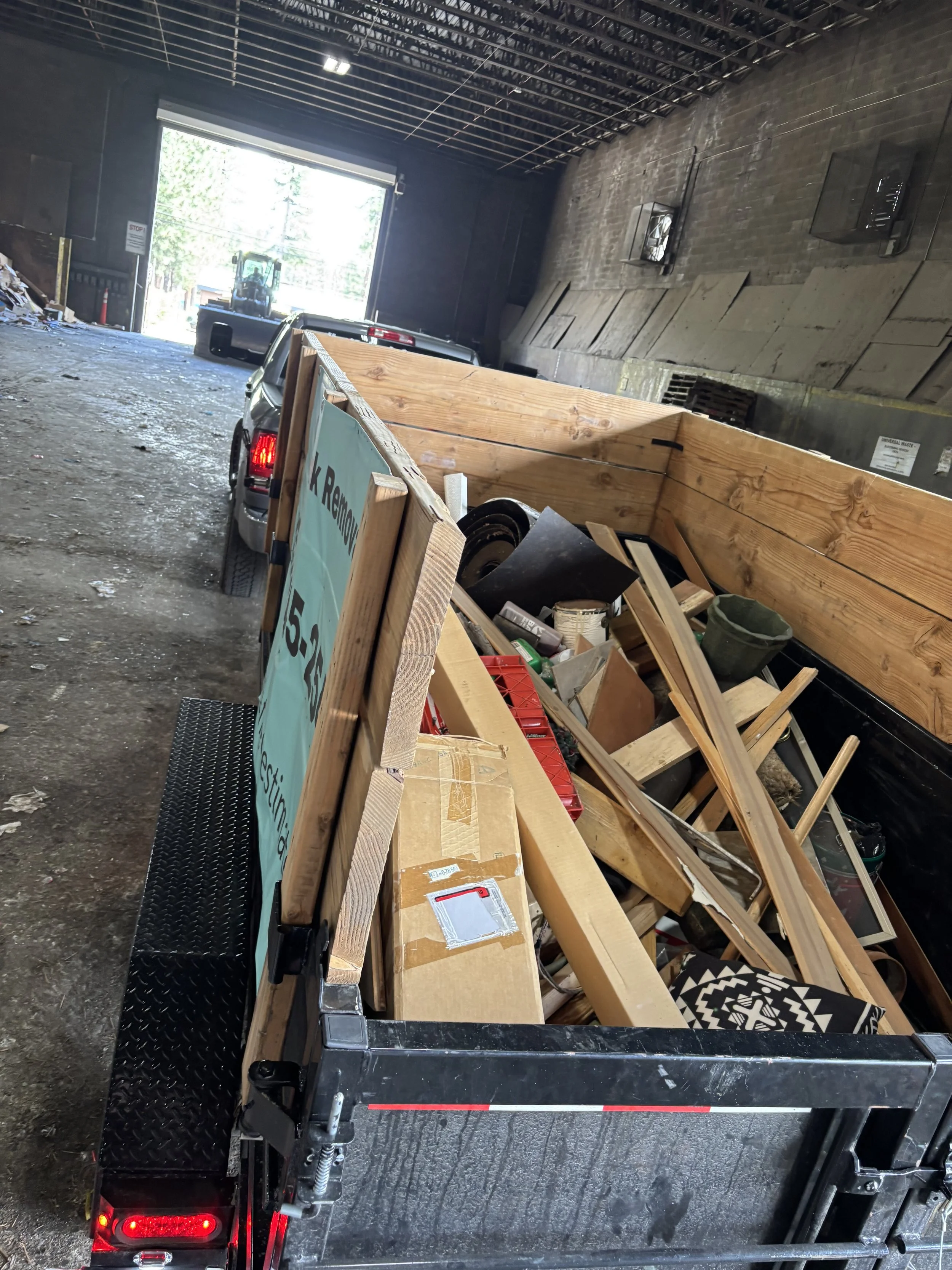 Inside a warehouse or loading dock, a black flatbed trailer parked with wooden planks and boxes on it, and a sign with some text partially visible.