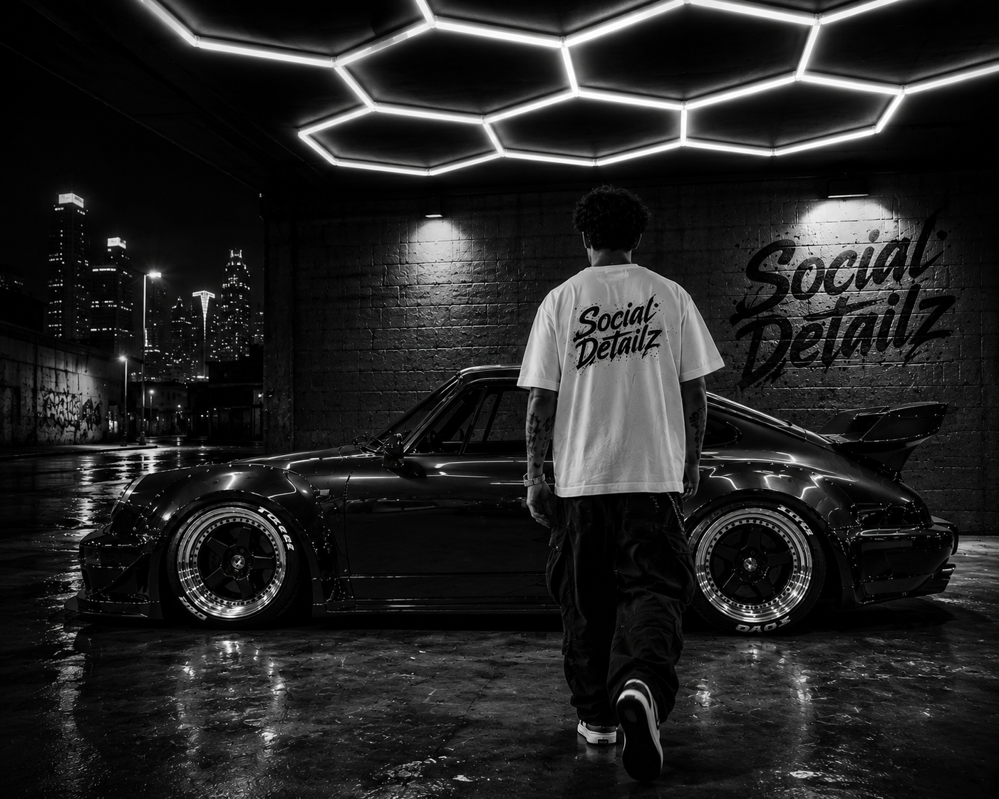 A person with tattoos wearing a white T-shirt with 'Social Detailz' written on the back, walking towards a black sports car in an urban, rainy night setting with city skyline and illuminated hexagon ceiling design.