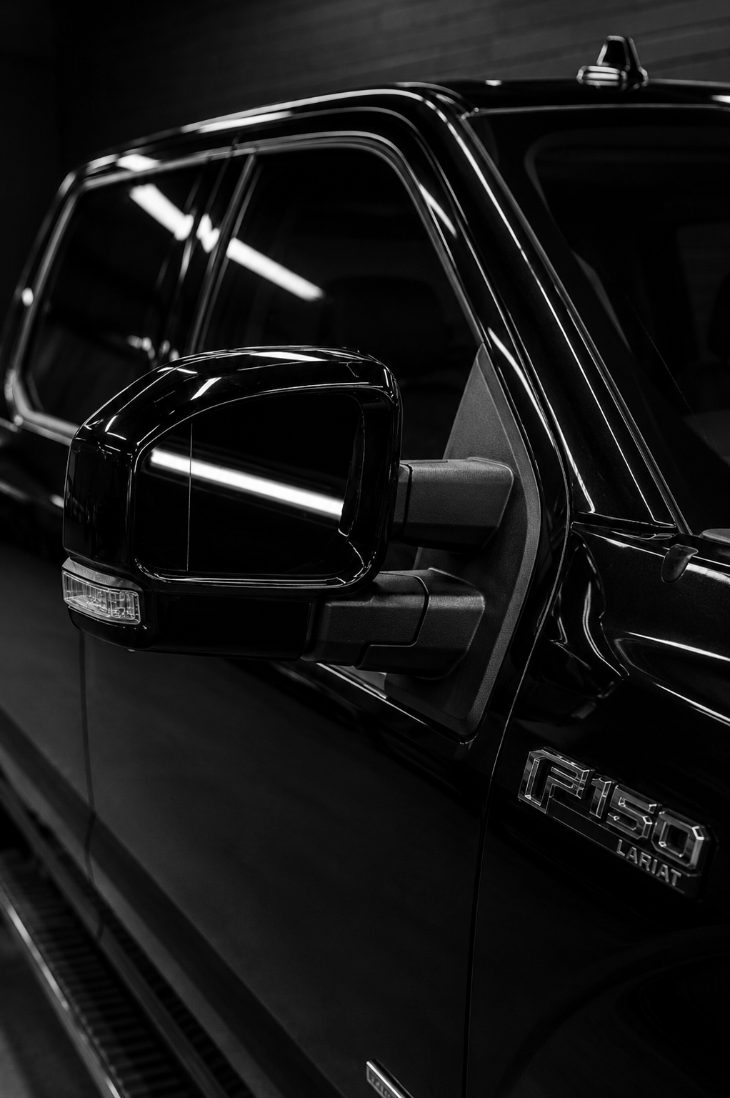 Close-up of a black Ford F-150 LARIAT pickup truck's side mirror and front door, displaying the vehicle's emblem.