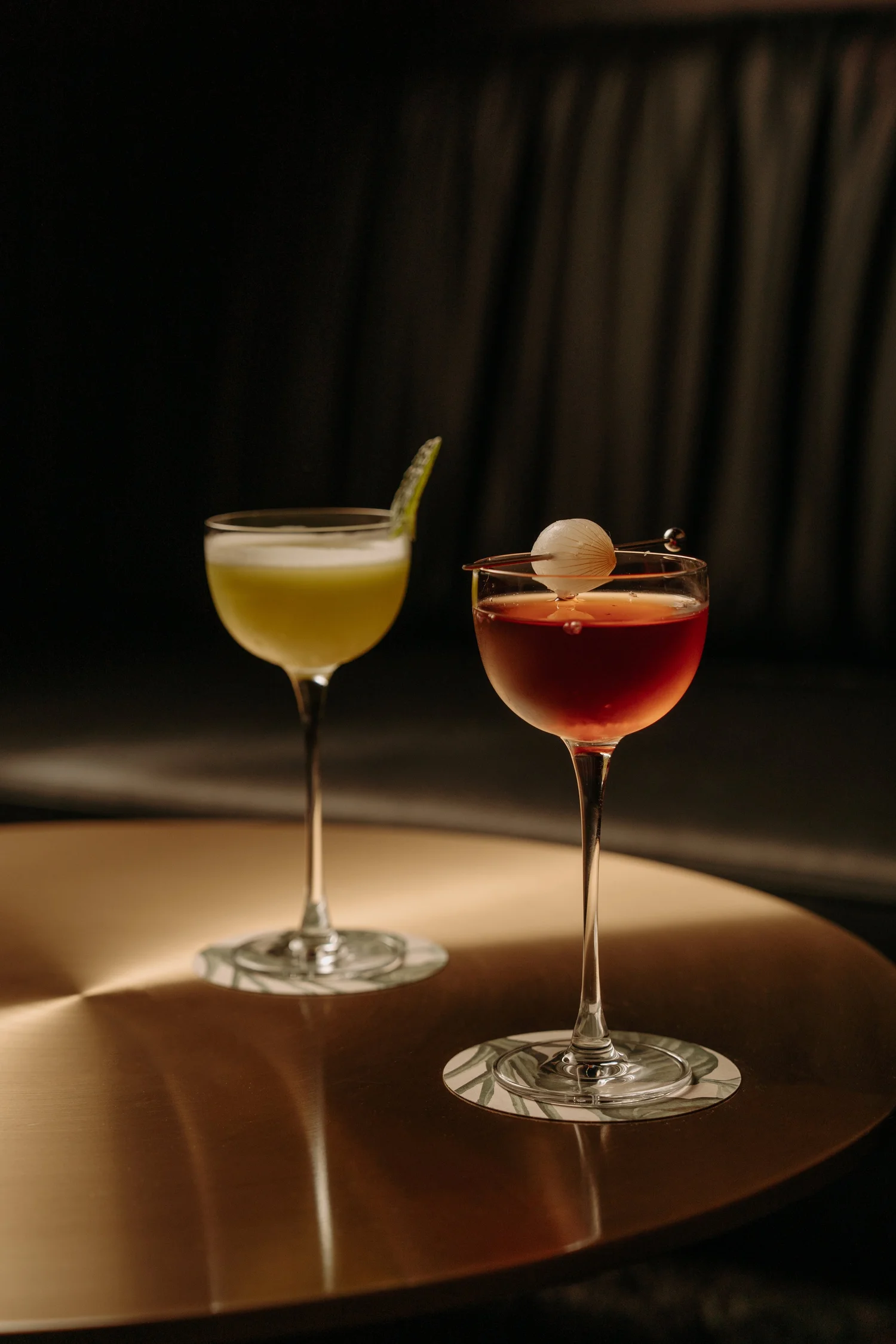 Two cocktails on a table in low light