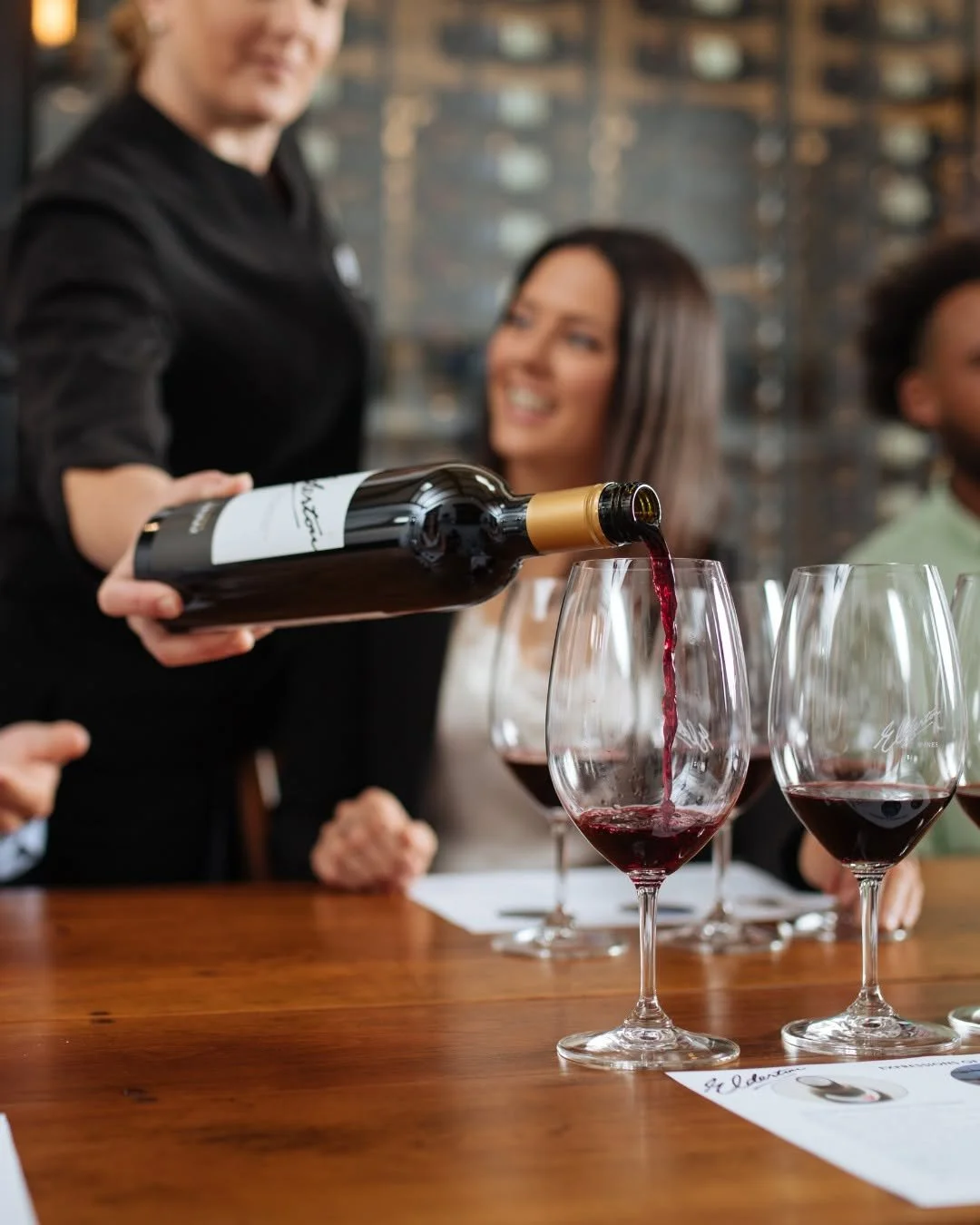An Elderton wine being poured for guests at a tasting table, red wine glasses catching the pour