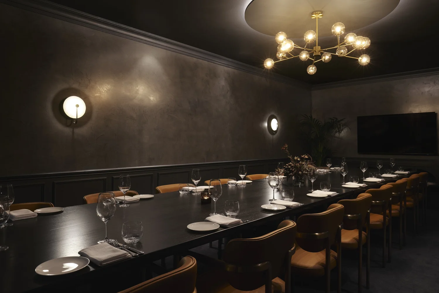 Private Dining Room 1 set for a long table dinner, with a wall-mounted screen for presentations