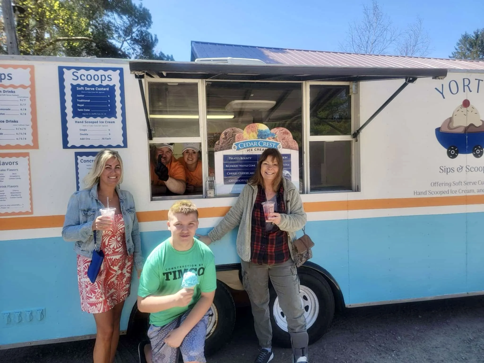 Four people, two women, one young boy, and a man inside an ice cream truck, enjoying ice cream cones on a sunny day outdoors.
