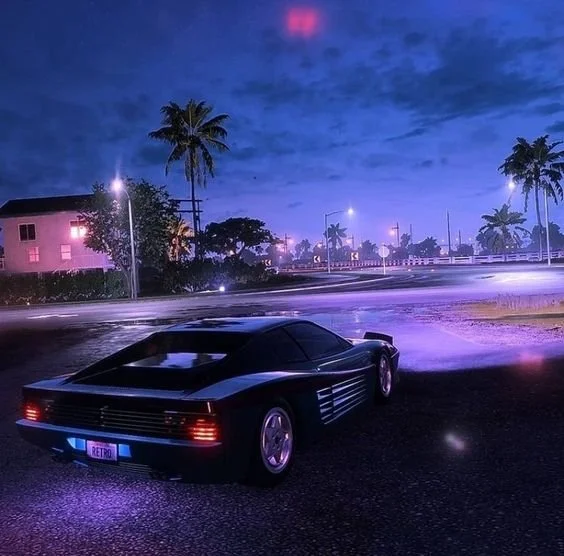 A black sports car with illuminated purple underglow parked on the side of a street at night, with palm trees, streetlights, and buildings in the background under a cloudy sky.