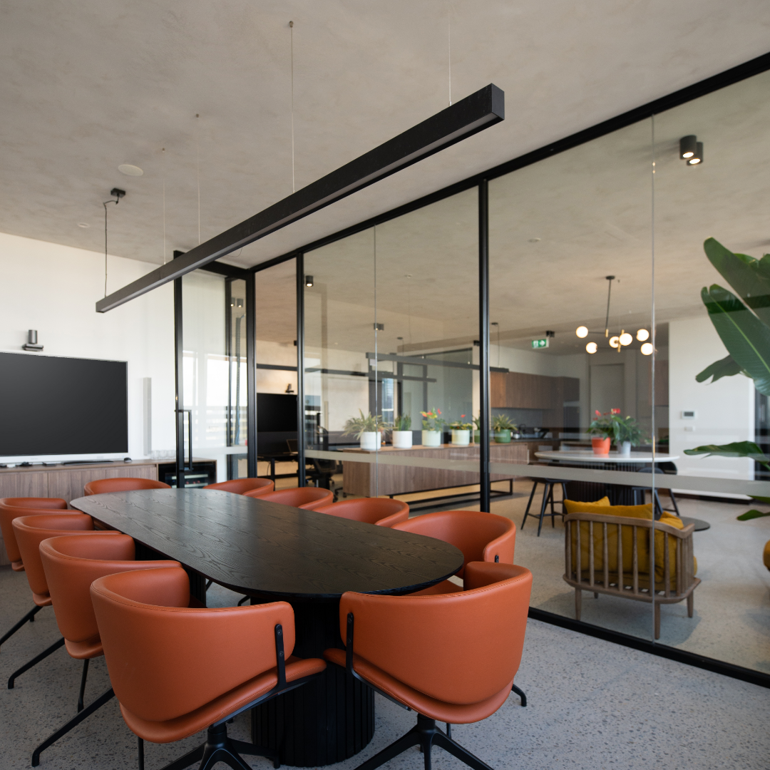 Modern open-concept living and dining area with a black oval table surrounded by orange chairs, glass partition, potted plants, and minimalist lighting.