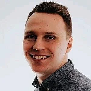 A young man with short brown hair and a friendly smile, wearing a gray shirt against a plain background.