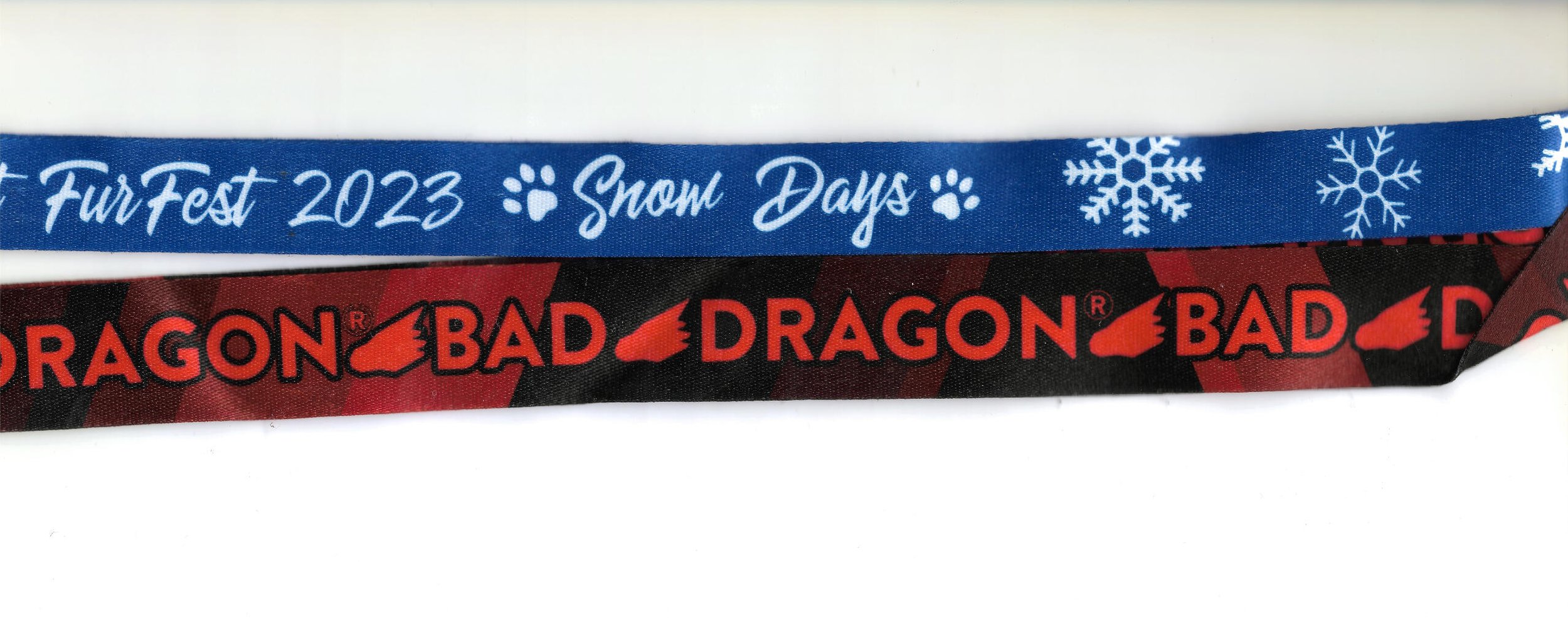 Blue lanyard with white snowflakes and text that reads "Fur Fest 2023 Snow Days." Black and red lanyard with the Red Dragon Bad logo.
