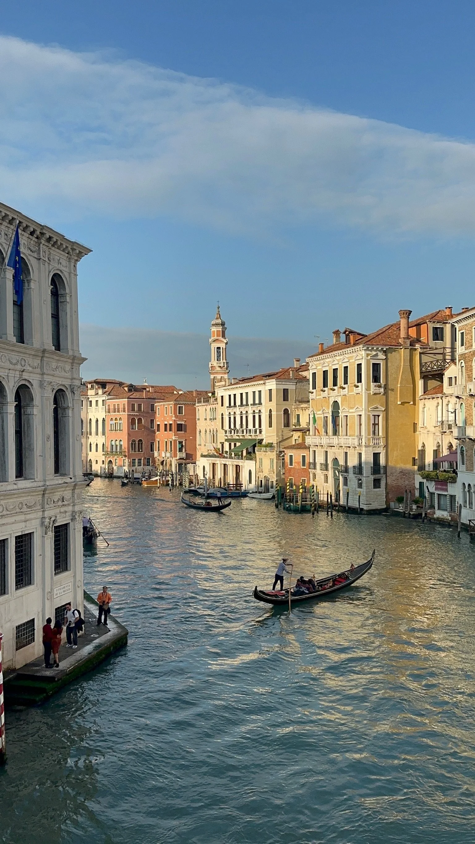 Gondola sailing through a canal in Venice, Italy, with historic buildings along the water and a blue sky overhead.
