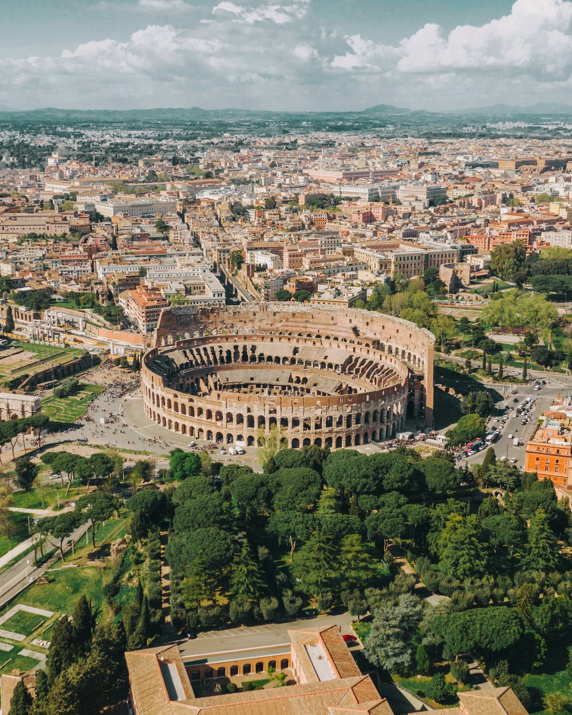 Aerial view of the Colosseum in Rome with surrounding cityscape and greenery.