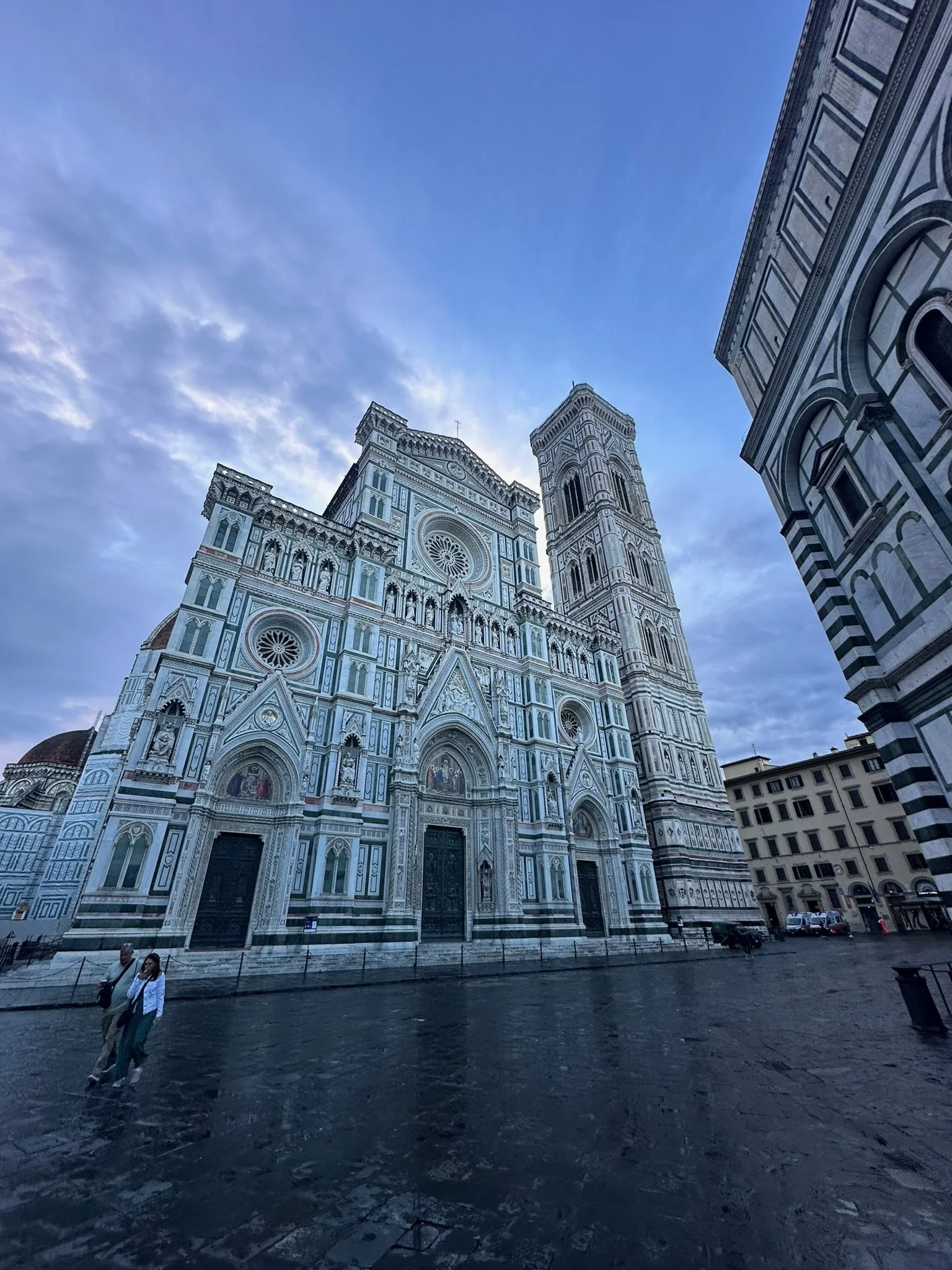 View of the Florence Cathedral (Santa Maria del Fiore) in Italy, showcasing its ornate marble facade and cathedral bell tower against a blue sky.