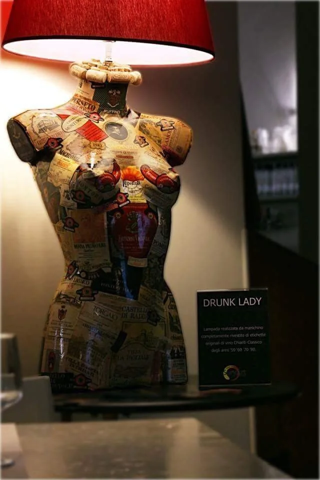 Una lampada a forma di torso femminile decorato con immagini di bottiglie di vino e etichette.