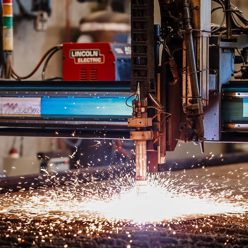 A CNC plasma cutting machine cutting metal, with sparks flying as it cuts through the material.