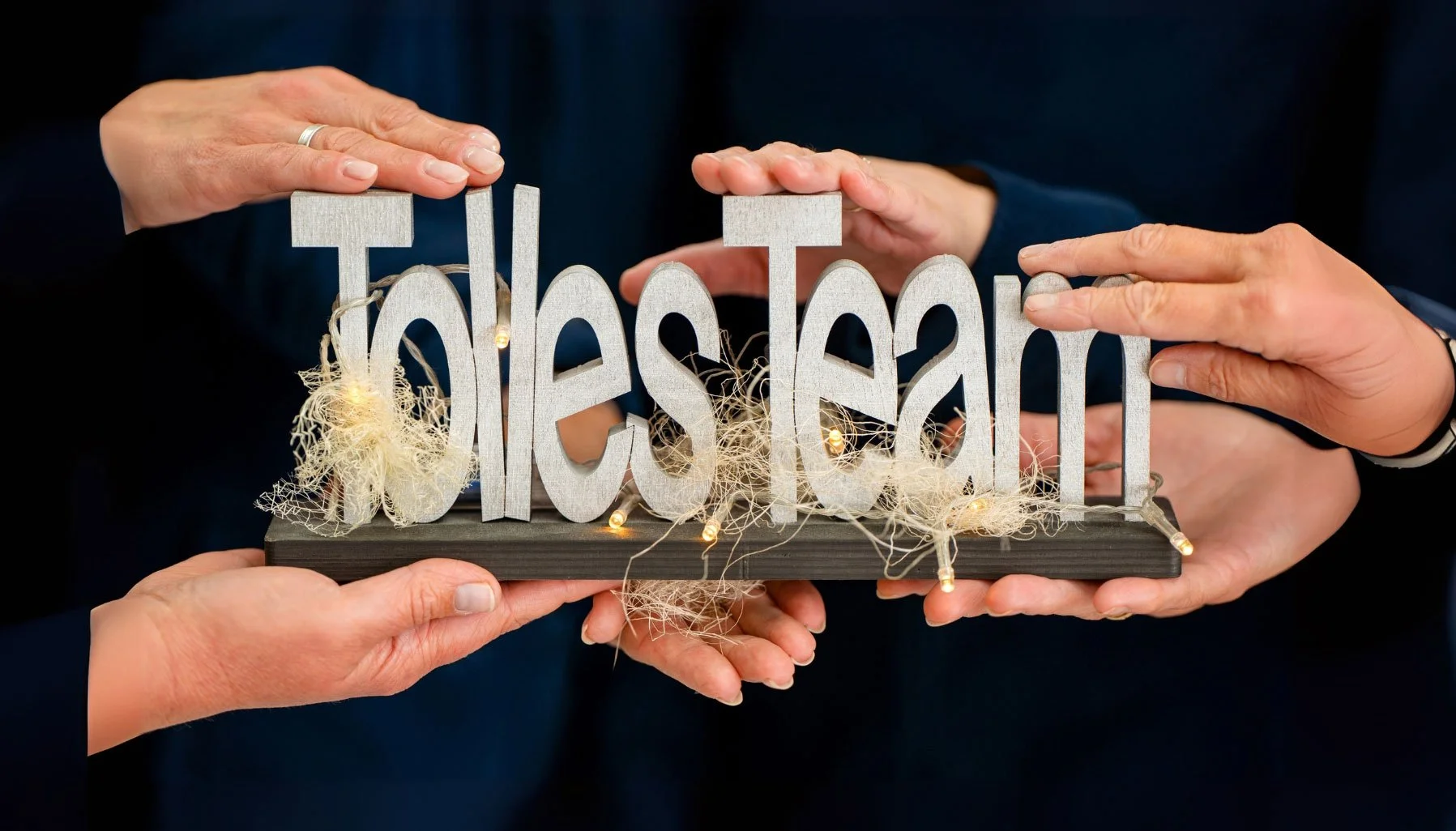 Mehrere Hände halten gemeinsam ein Schild mit der Aufschrift „Tolles Team“