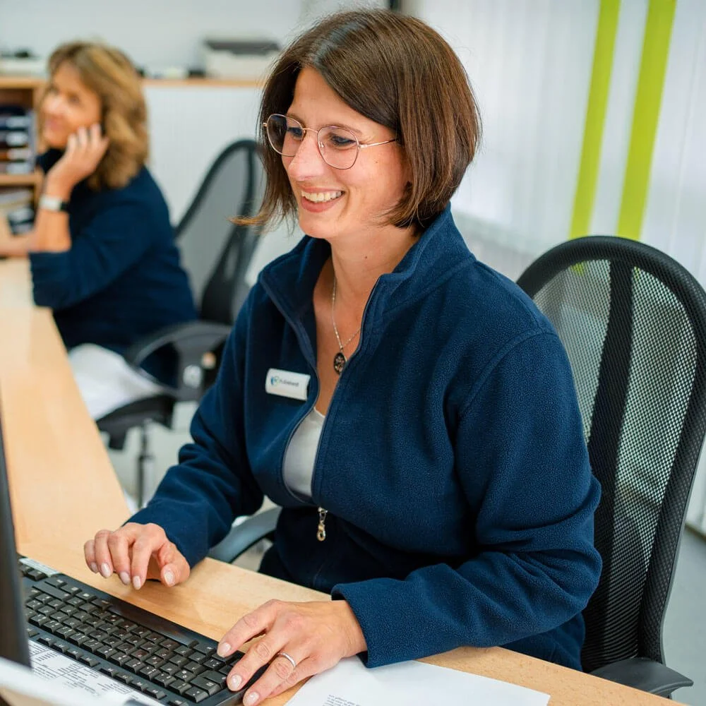 Frau Enkhardt am Empfang, lächelnd am Computer