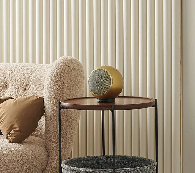 Ein runder Lautsprecher auf einem kleinen Tisch neben einem Sofa mit Kissen, im Hintergrund beige Vorhänge.