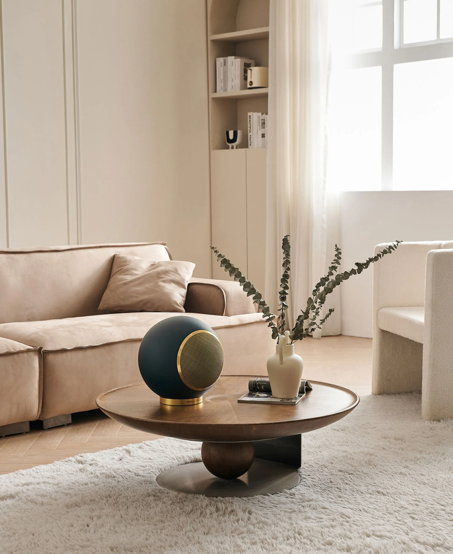 Moderner Wohnzimmer mit braunem Sofa, Holztisch, weißen Vorhängen, Bücherregal, Topf mit grünen Zweigen und einer schwarzen Lautsprecherbox.