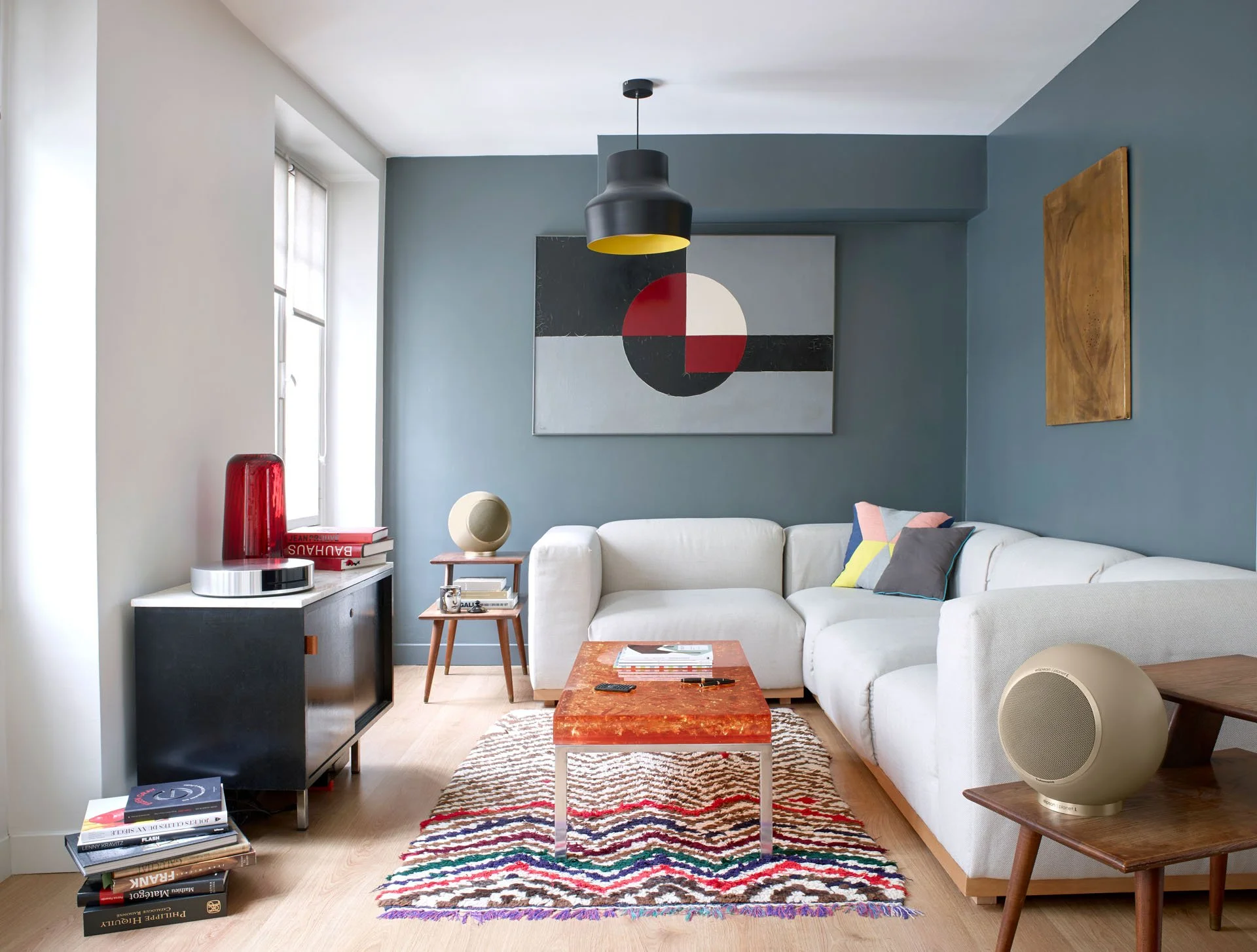 Moderner Wohnzimmer mit blauer Wand, weißem Sofa, buntem Teppich, Wandkunst, dunklem Lampenschirm, Holz- und modernen Dekorationen.