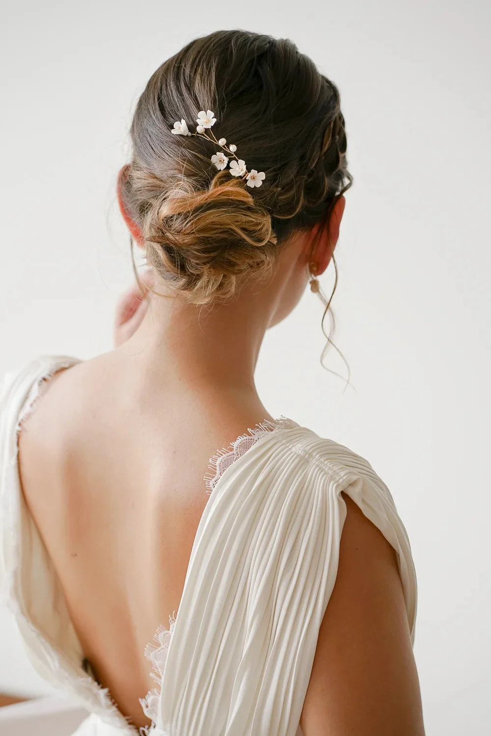 Coiffure de mariée avec chignon élégant et décoration florale blanche, fabriquée par la marque Atelier Lilac.