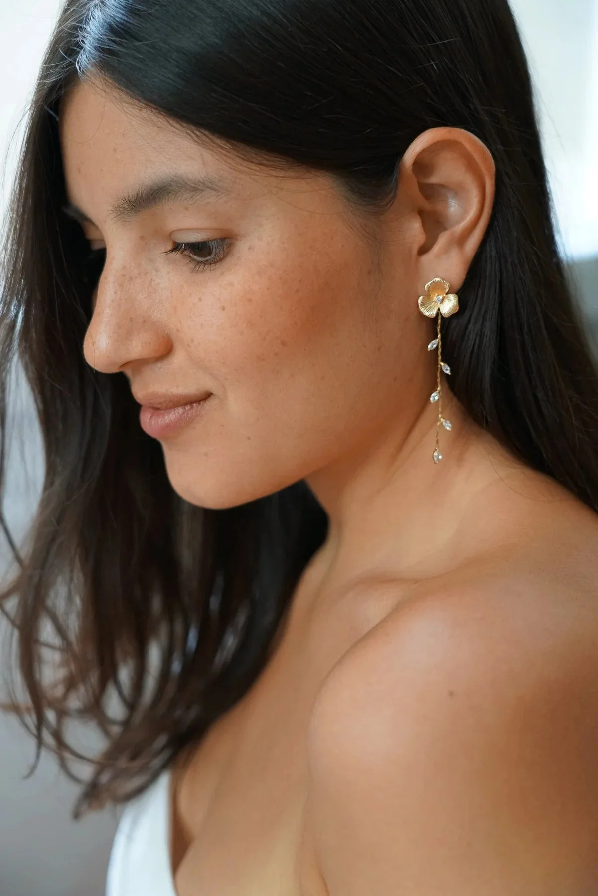 Femme portant une boucle d'oreille en forme de fleur en or avec des détails en perles et des pierres en forme de goutte d'eau par la marque Atelier Lilac.
