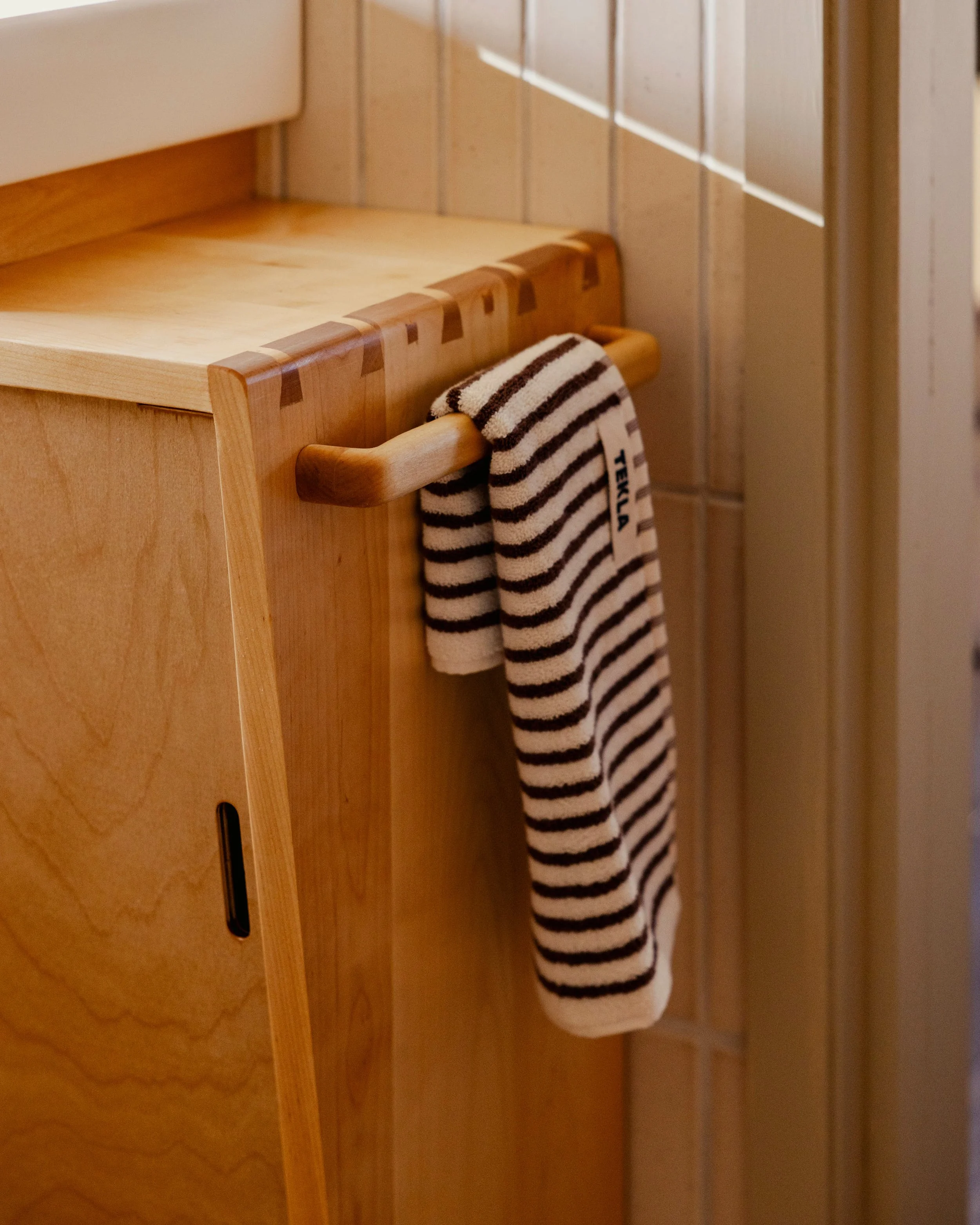 A striped towel hanging on a wooden towel rack in a bathroom with wood-paneled walls.