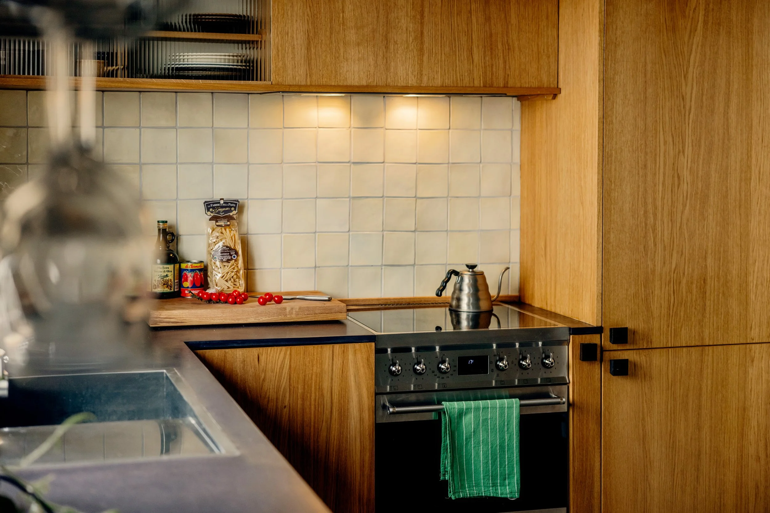 Oak kitchen in Oslo with fluted glass top cabinets and valchromat kitchen worktop. Natural light filtering through yellow waveband curtains. 1940s 1970s style interior. Studio Dahl tiles on backsplash. Built by EZRA MEADEN. 