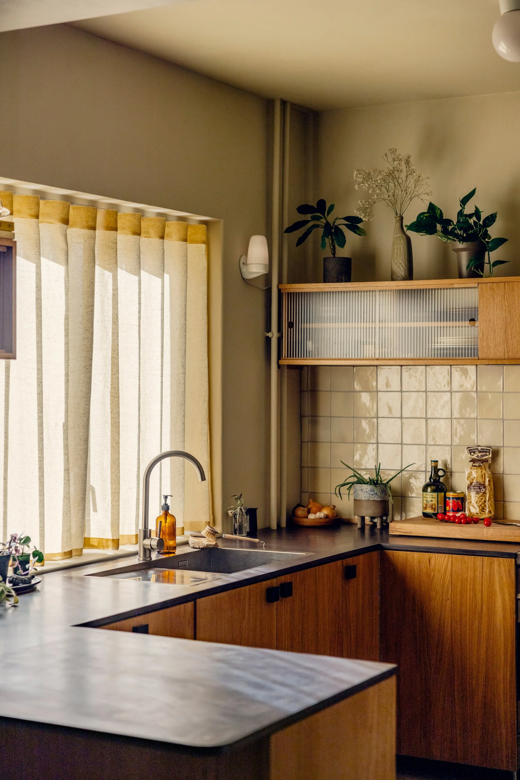 Oak kitchen in Oslo with fluted glass top cabinets and valchromat kitchen worktop. Natural light filtering through yellow waveband curtains. 1940s 1970s style interior. Studio Dahl tiles on backsplash. Built by EZRA MEADEN. 
