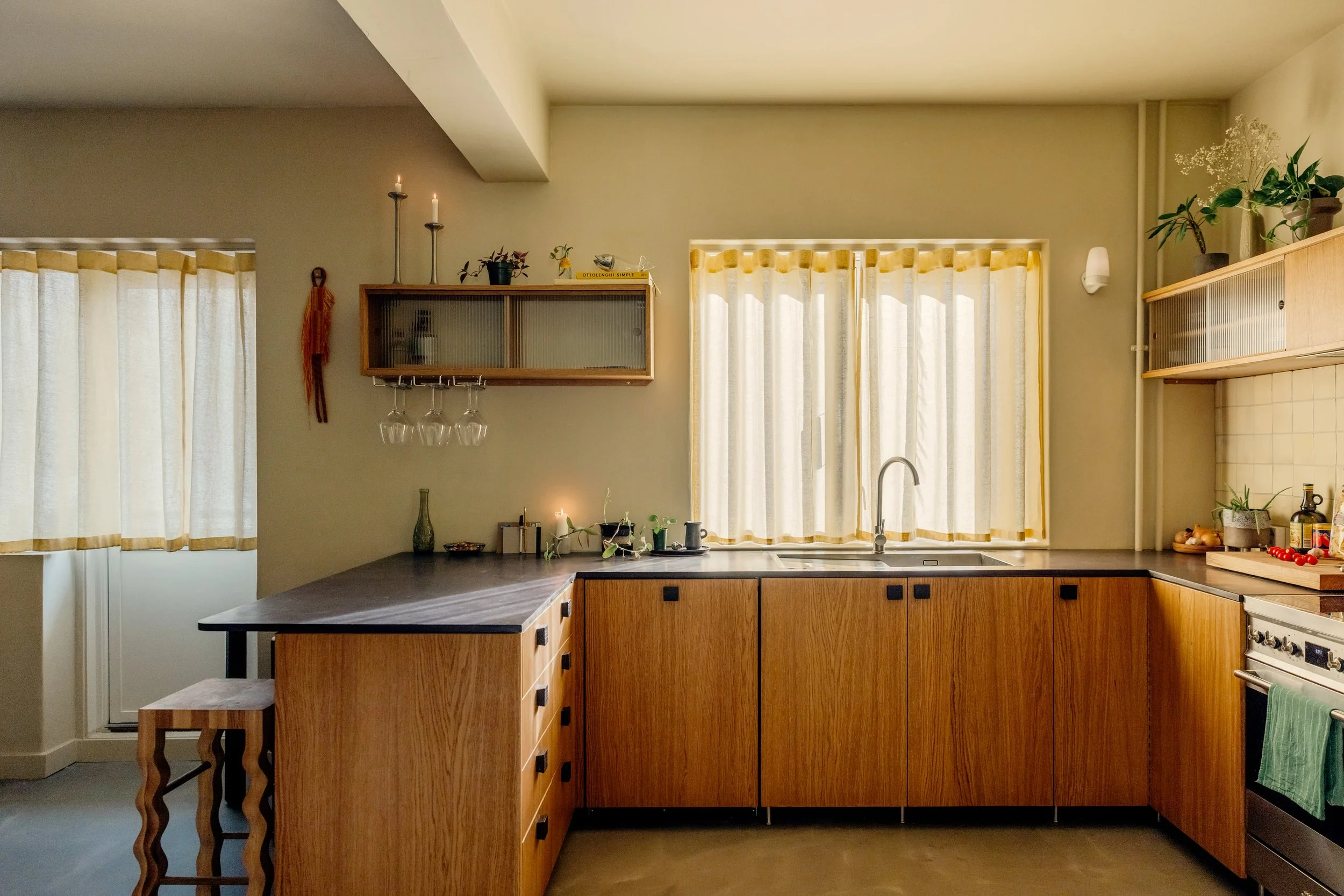 Oak kitchen in Oslo with fluted glass top cabinets and valchromat kitchen worktop. Natural light filtering through yellow waveband curtains. 1940s 1970s style interior. Studio Dahl tiles on backsplash. Built by EZRA MEADEN. 