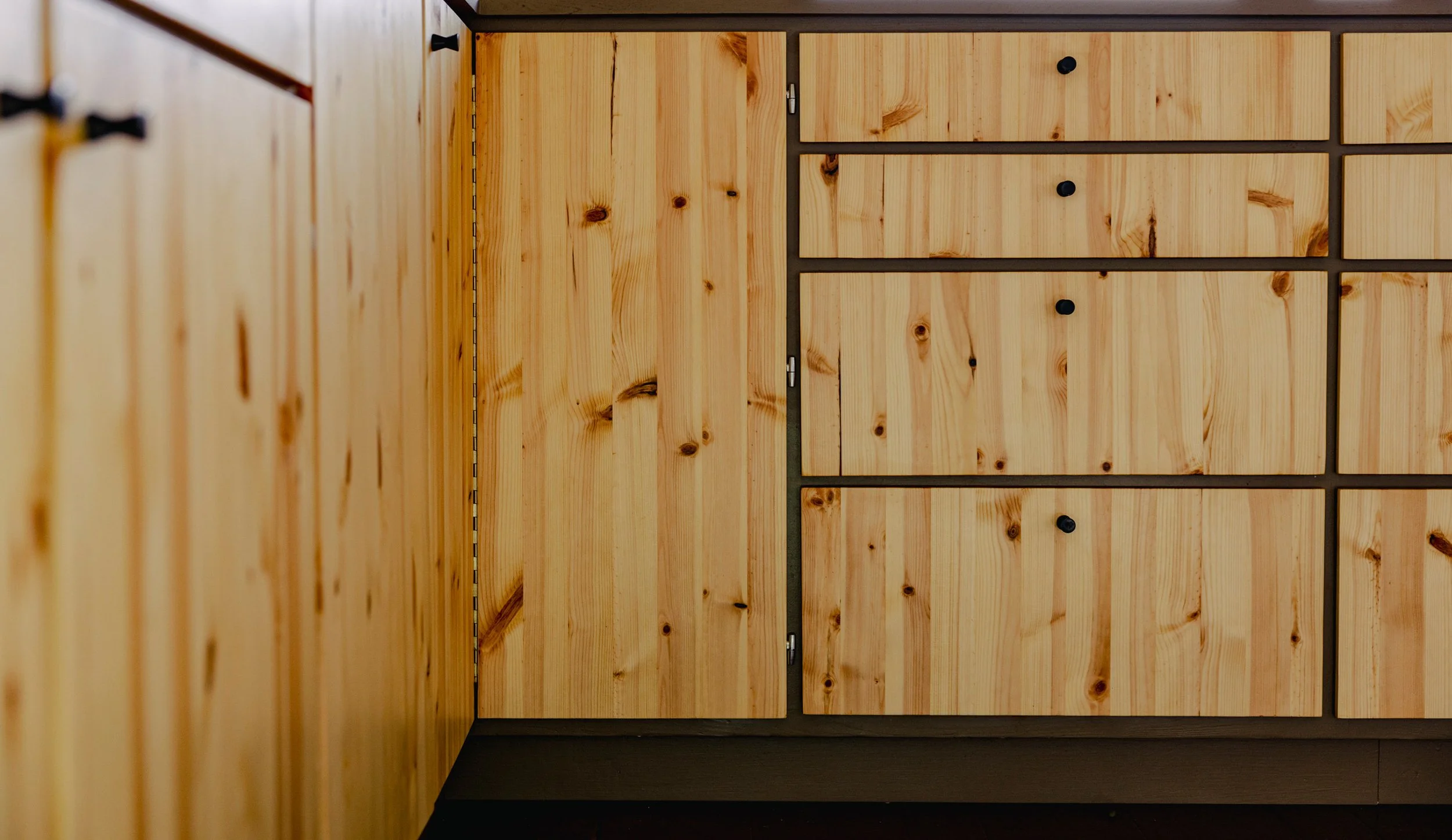 View of wooden cabinets with black knobs, set in a room with dark flooring.