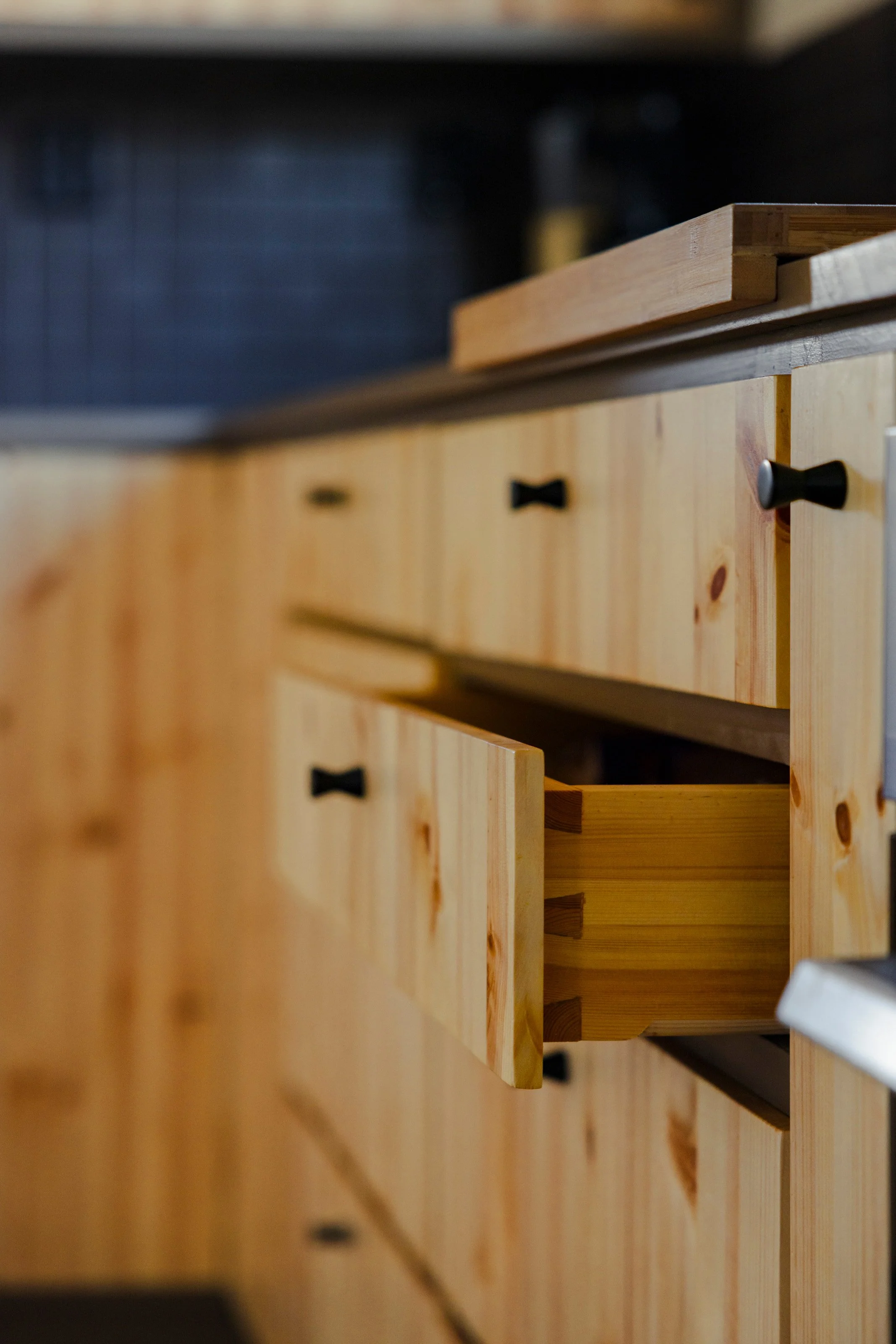 Close-up of wooden kitchen drawers with black knobs and a small wooden cutting board placed on top.