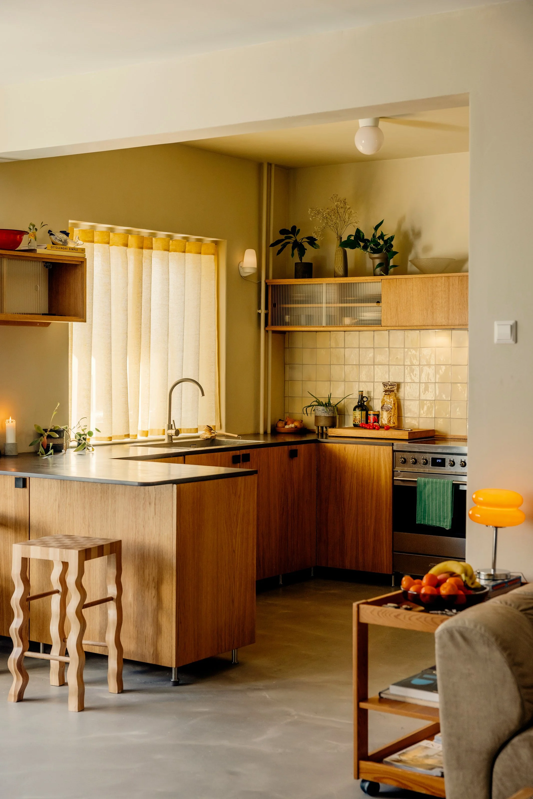 Oak kitchen in Oslo with fluted glass top cabinets and valchromat kitchen worktop. Natural light filtering through yellow waveband curtains. 1940s 1970s style interior. Studio Dahl tiles on backsplash. Built by EZRA MEADEN. 