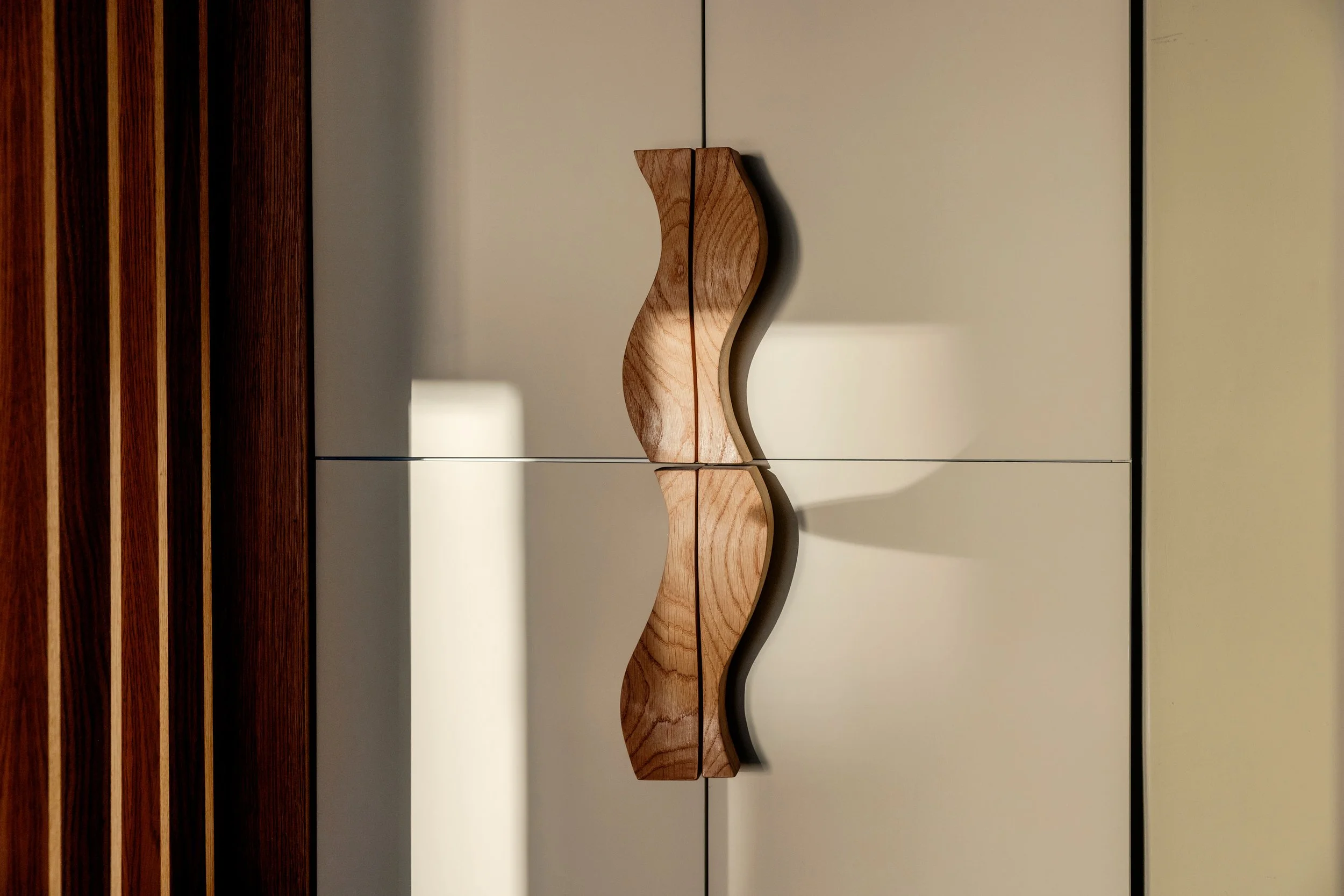 A wooden decorative piece with a curved, wave-like shape mounted on a white cabinet door.