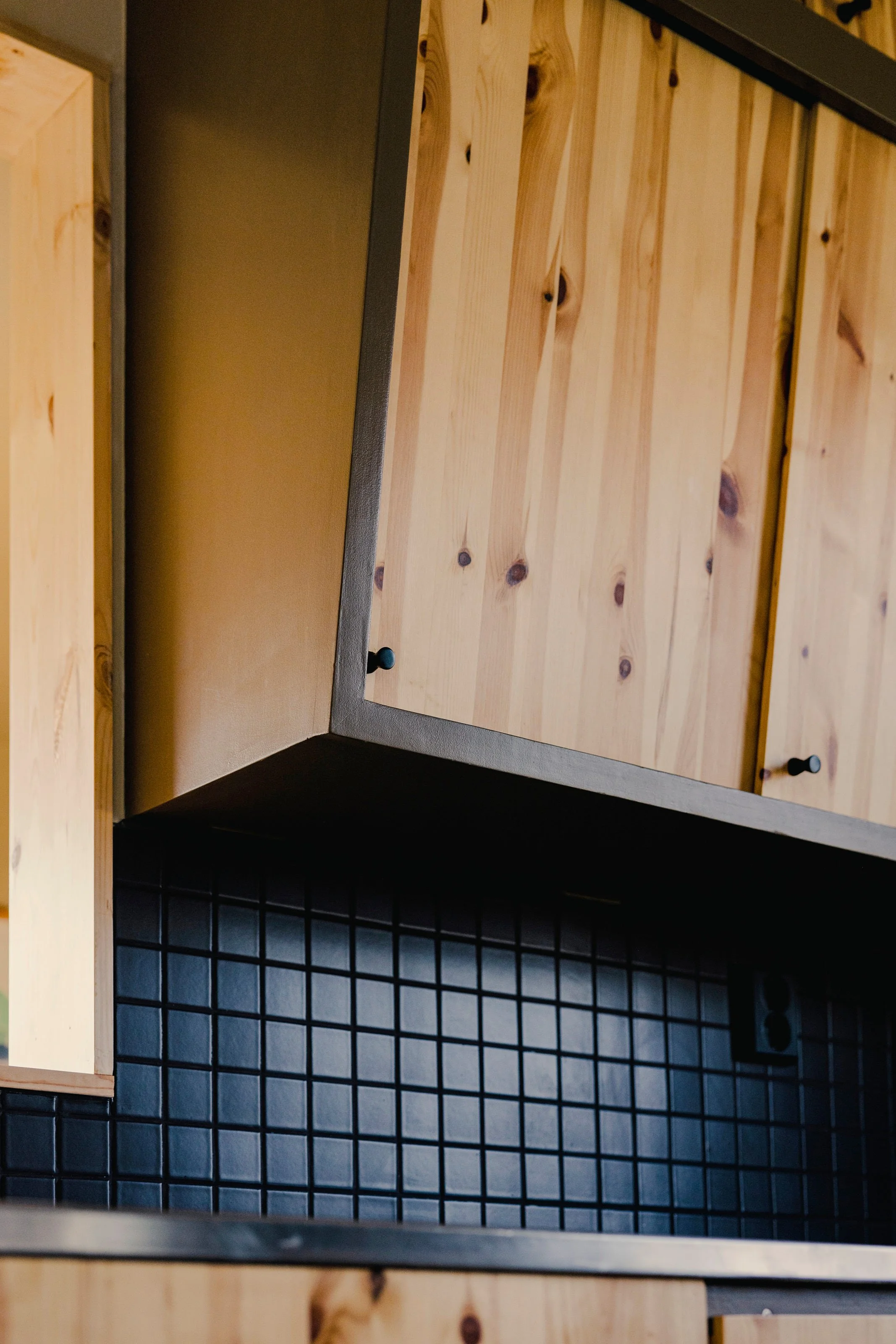 Close-up photo of a black wire grid storage basket, placed below an open wooden cabinet or shelf with visible wood grain and knots.