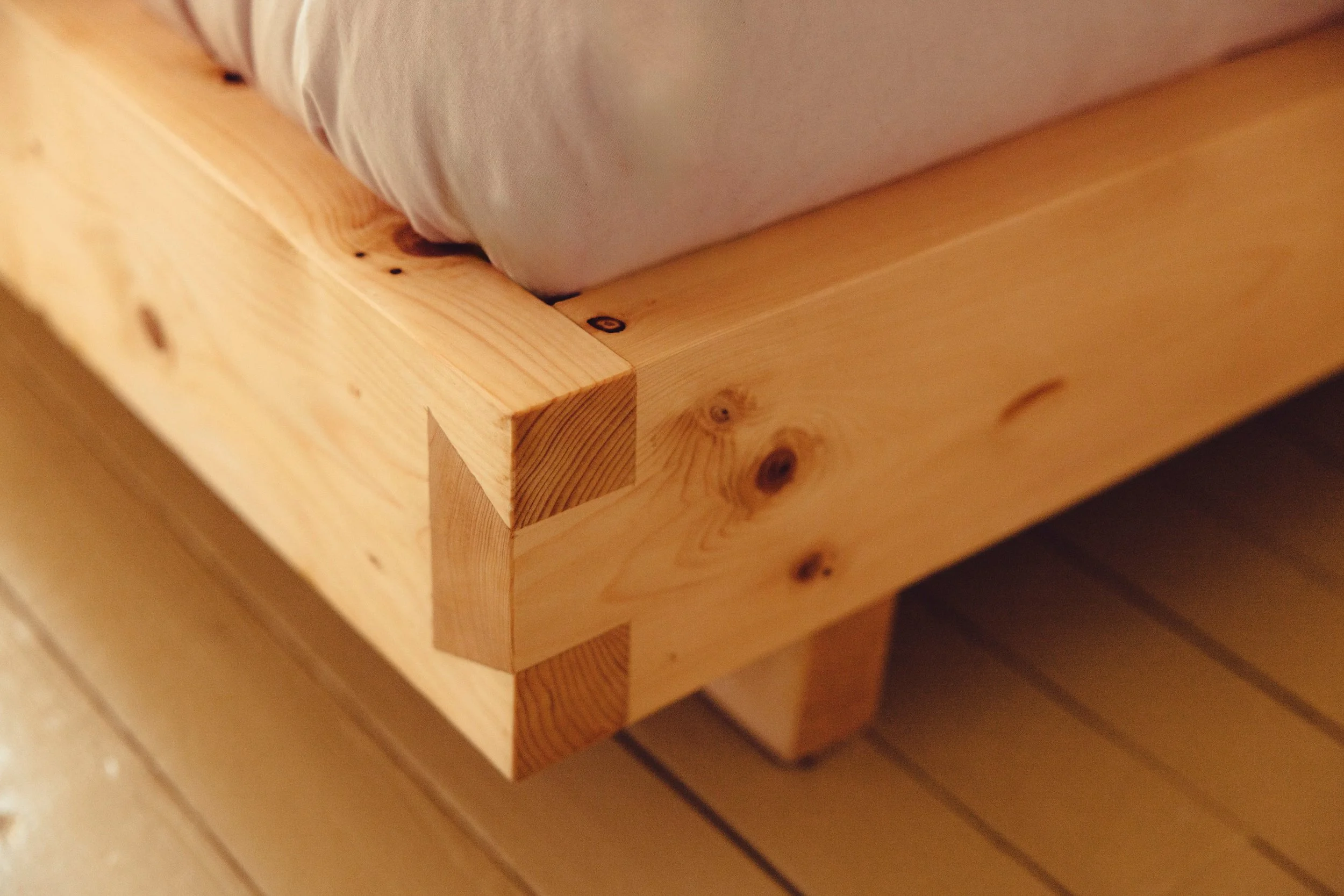 Close-up of a wooden bed frame with a mattress on top, showing the natural wood grain and knots.