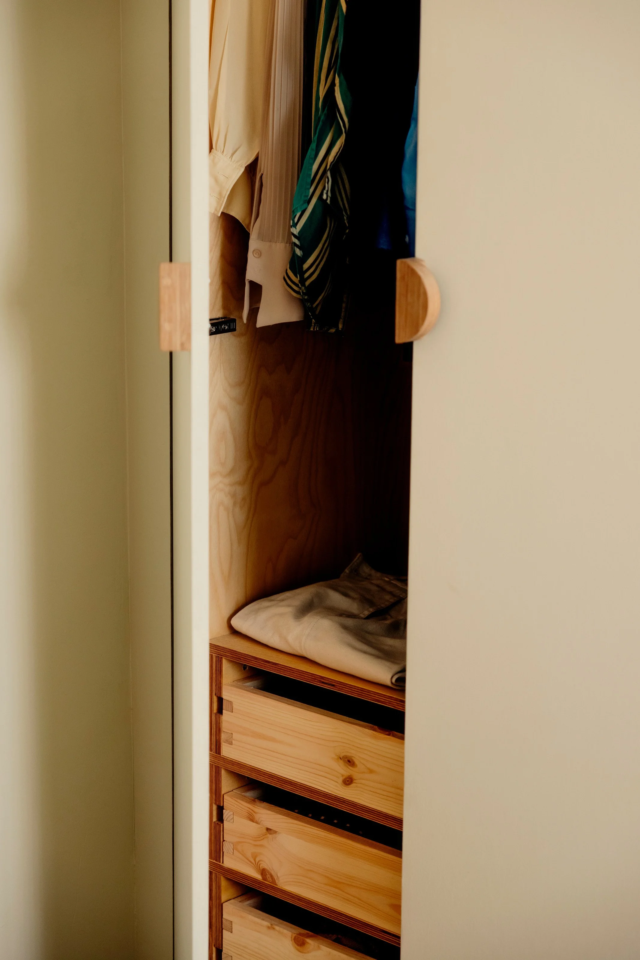 Open closet with wooden drawers, some clothes hanging and a mattress on the floor inside.