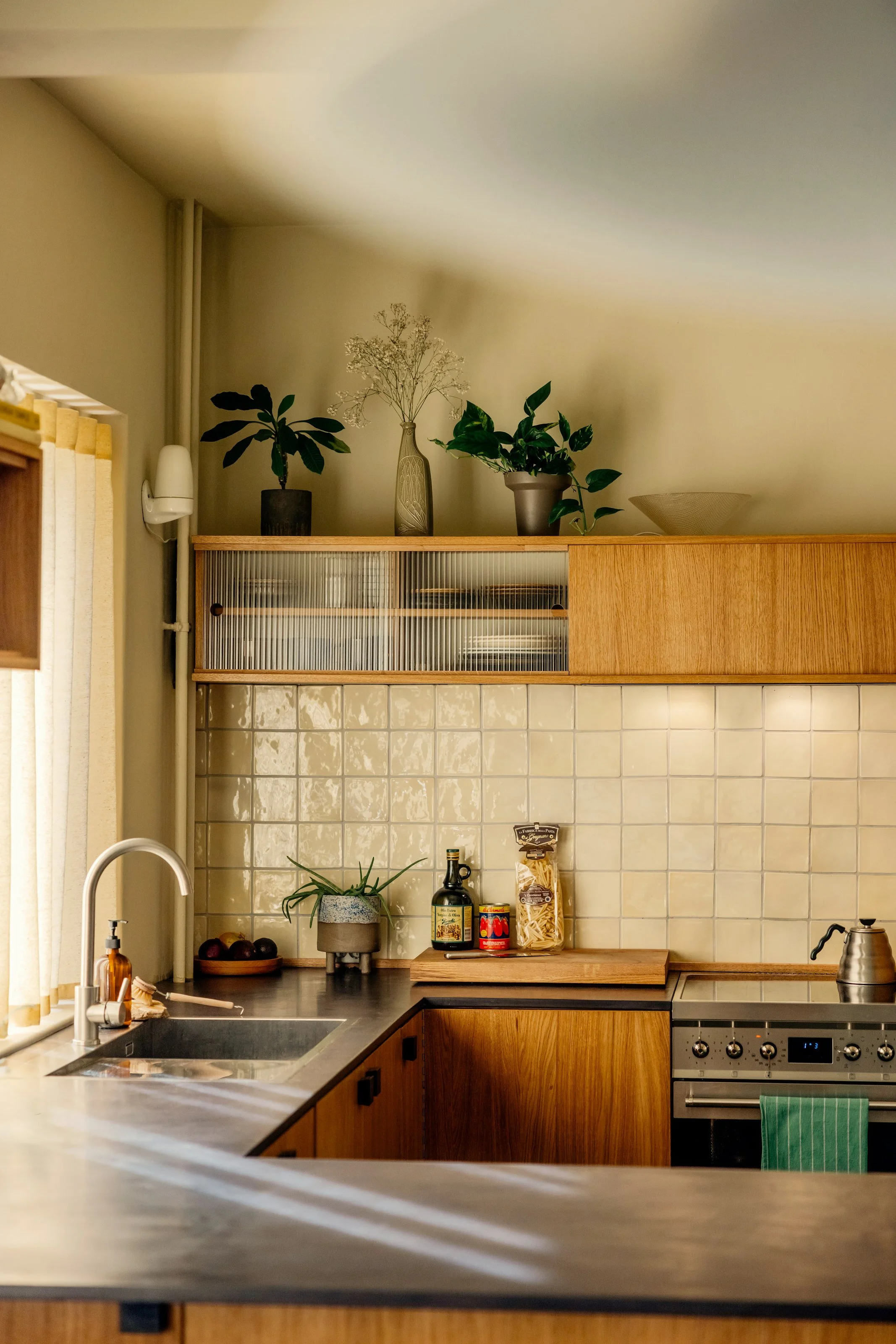 Oak kitchen in Oslo with fluted glass top cabinets and valchromat kitchen worktop. Natural light filtering through yellow waveband curtains. 1940s 1970s style interior. Studio Dahl tiles on backsplash. Built by EZRA MEADEN. 