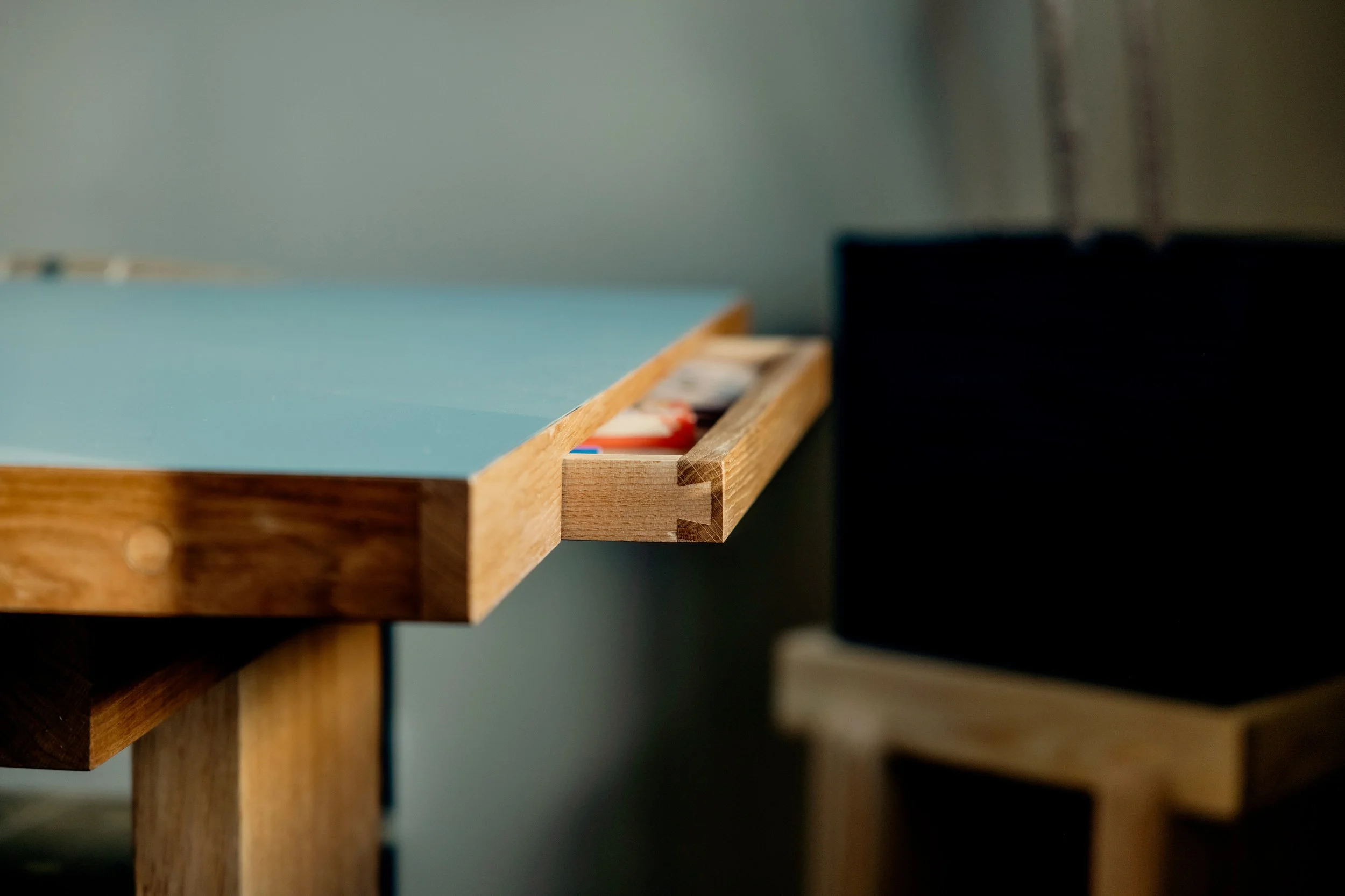 Close-up of a wooden drawer slightly pulled out, revealing some items inside, with a muted teal wall in the background.