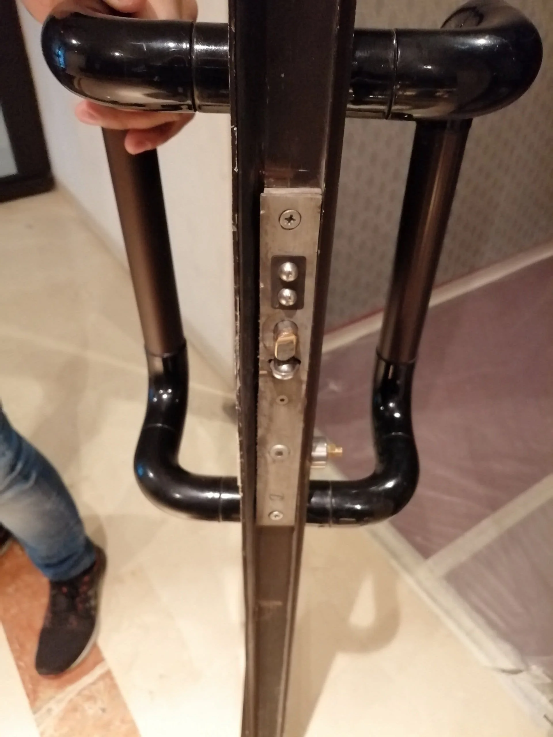 Porte avec poignée en métal noir et mécanisme de serrure, vue en gros plan.