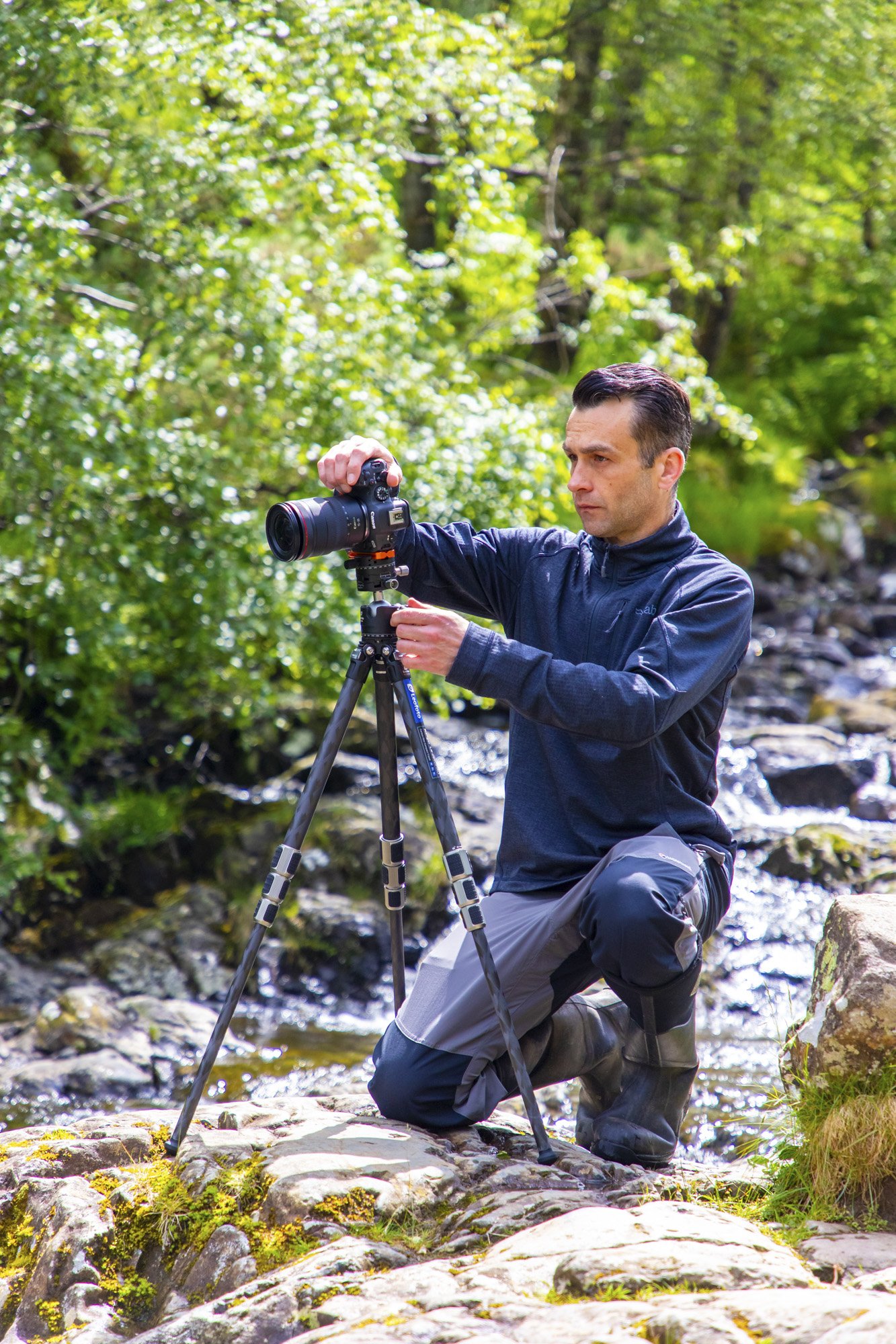 Professional landscapes photographer James Abbott has his camera set up on a tripod outdoors and is kneeling down taking pictures.