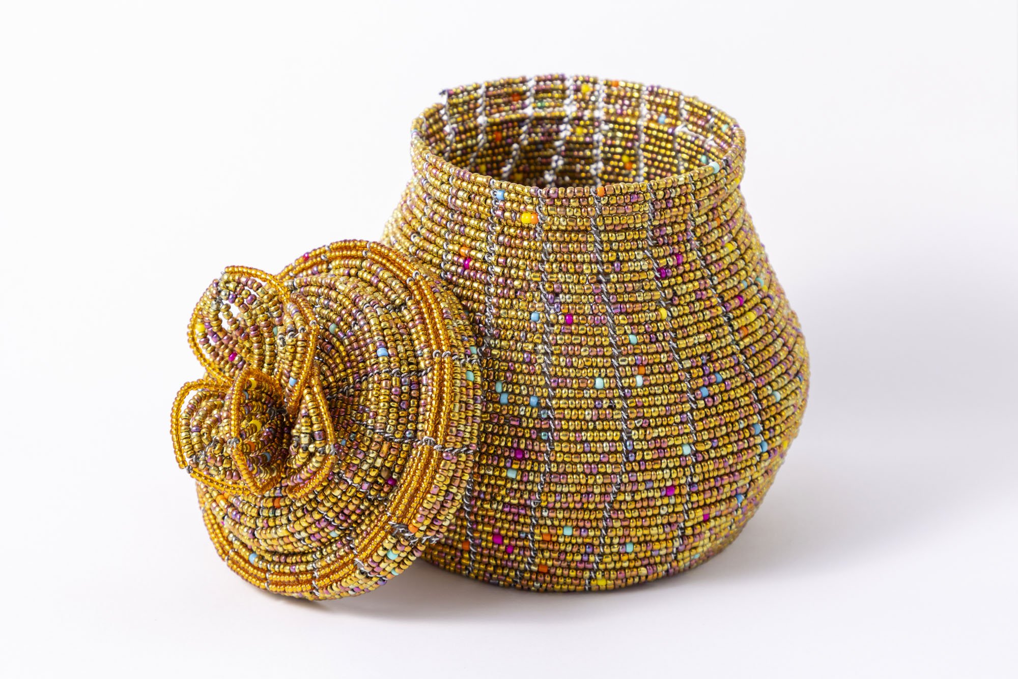 A professional product photo of a handmade beaded vase shot on white with its lid taken off and leaning against it.