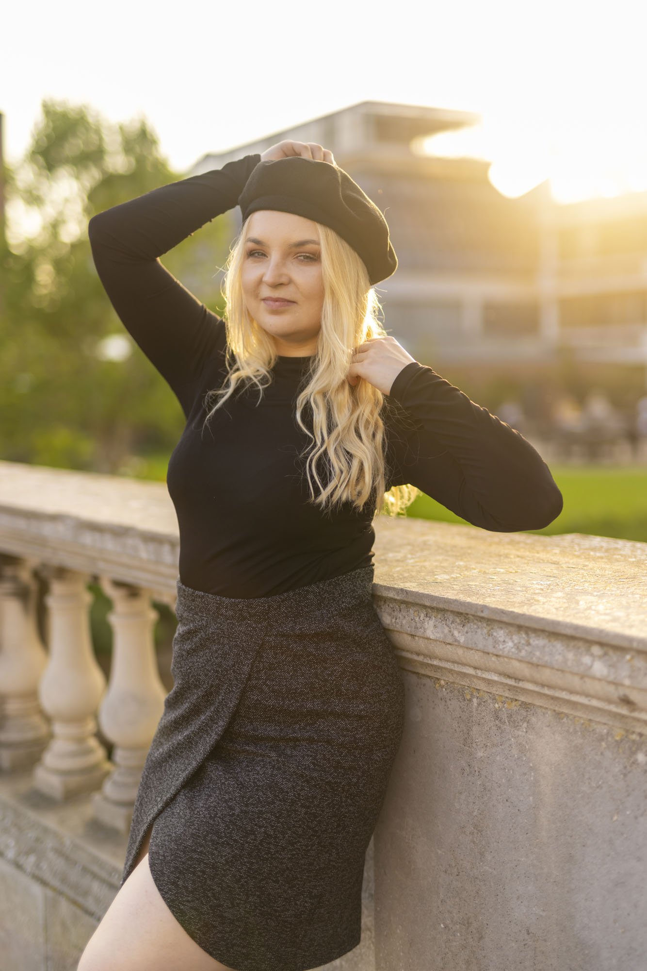 Model Rose Ford is posing leaning back on a stone bridge in Cambridge and is backlit by the low setting sun which has backlit her and added flare. She's wearing a dark grey and black outfit with a French style using a beret, turtleneck and pencil ski