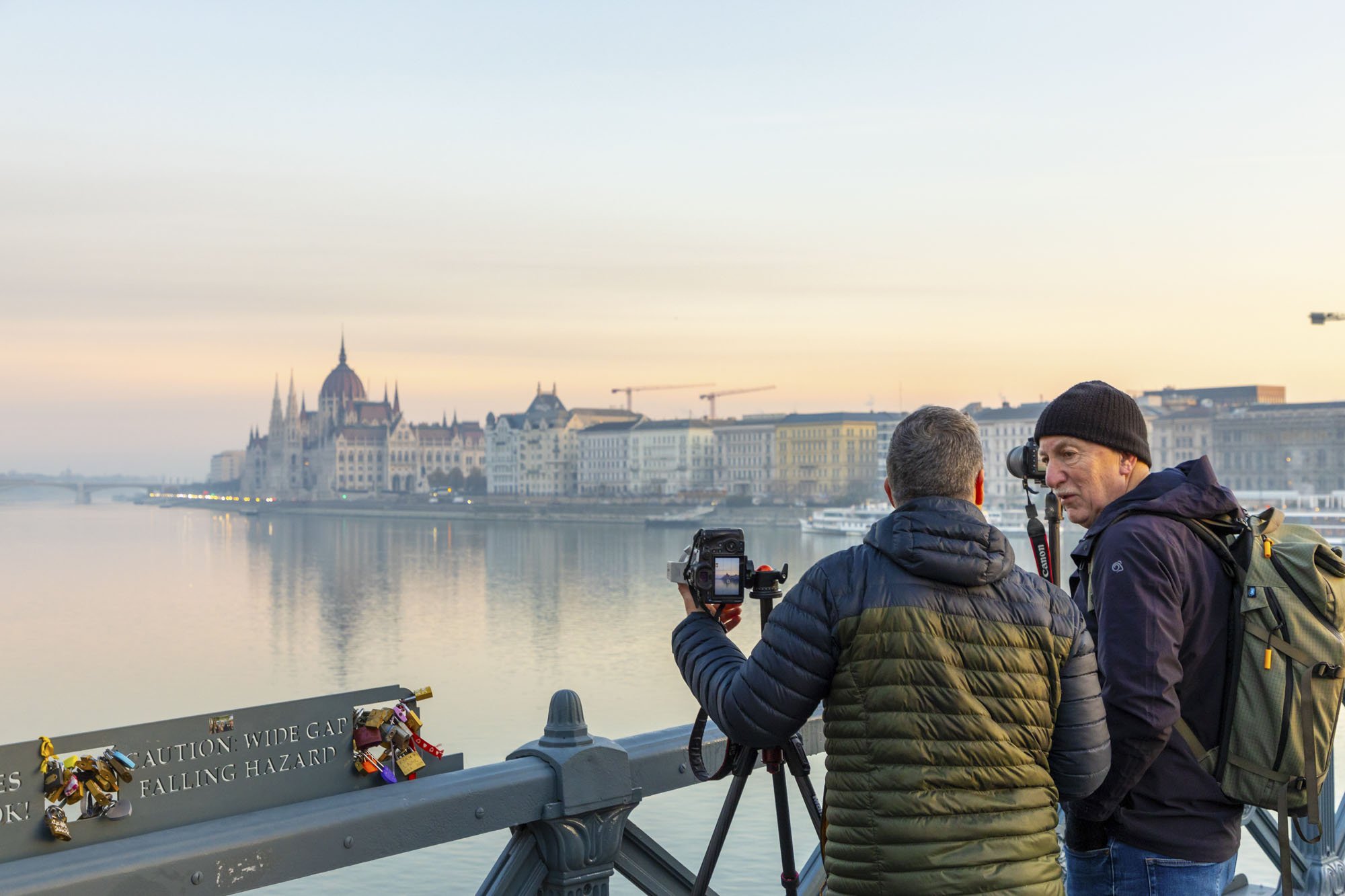 A picture of the Hungarian Parliament at sunrise with two photographers in the foreground using their cameras set up on tripods.