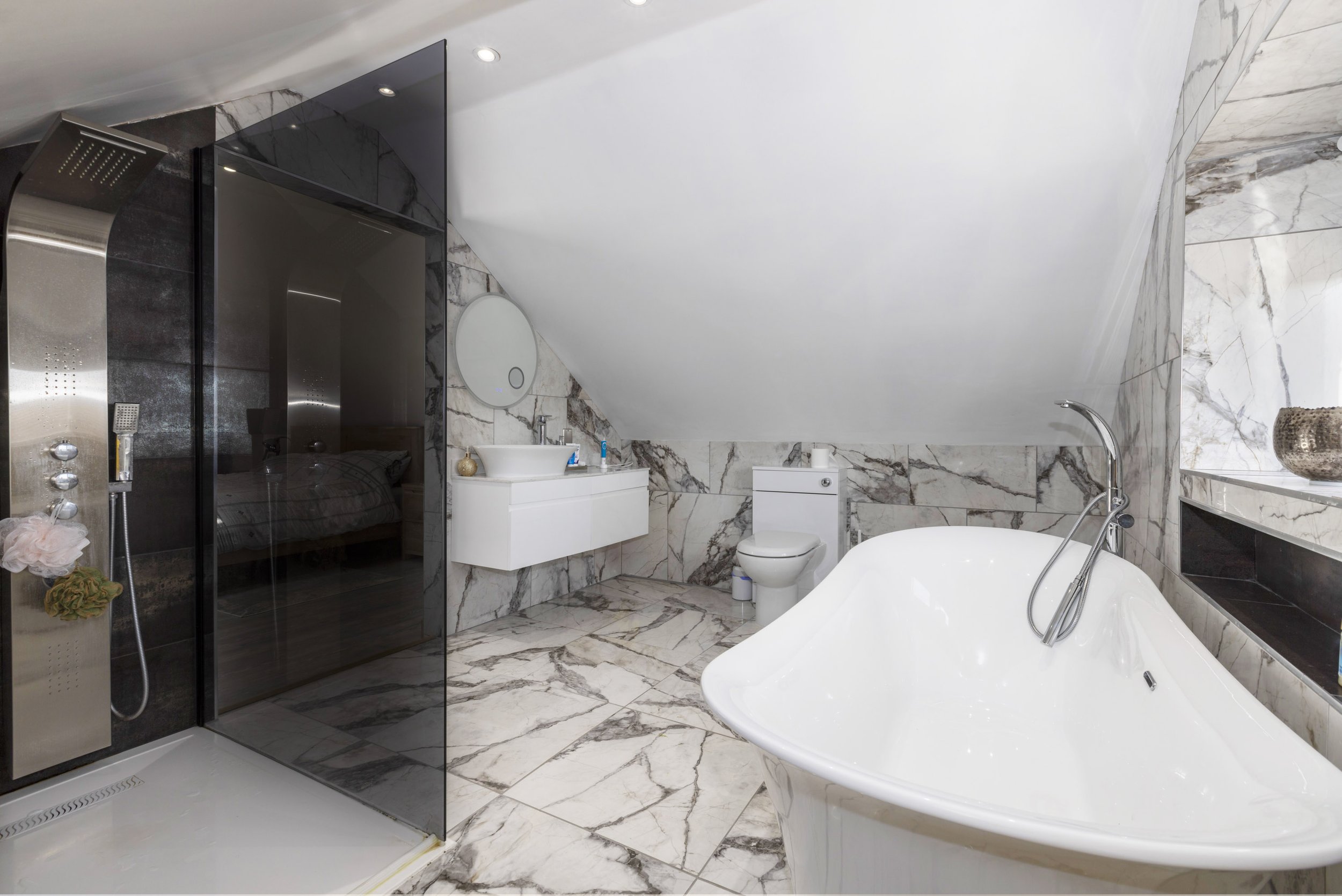 A clean bathroom with white marbled tiling, shower and bath.